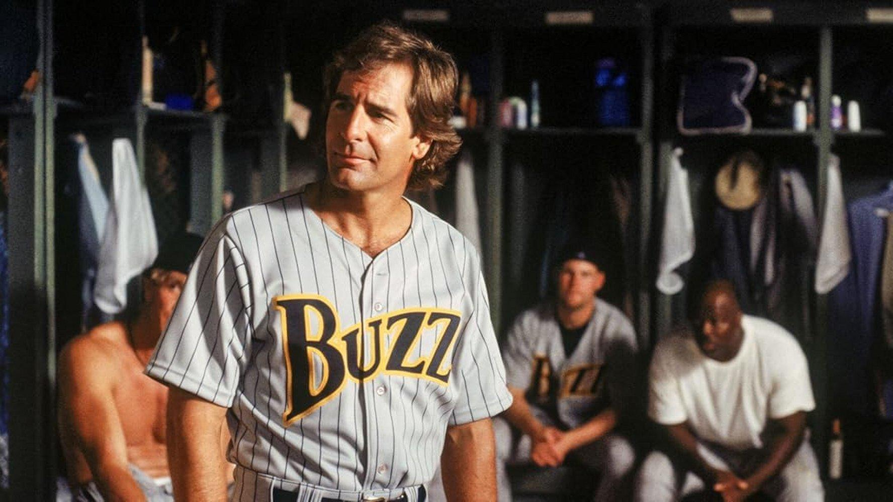 Ein Mann im Baseball-Trikot steht vor Umkleidespinden mit anderen Spielern.