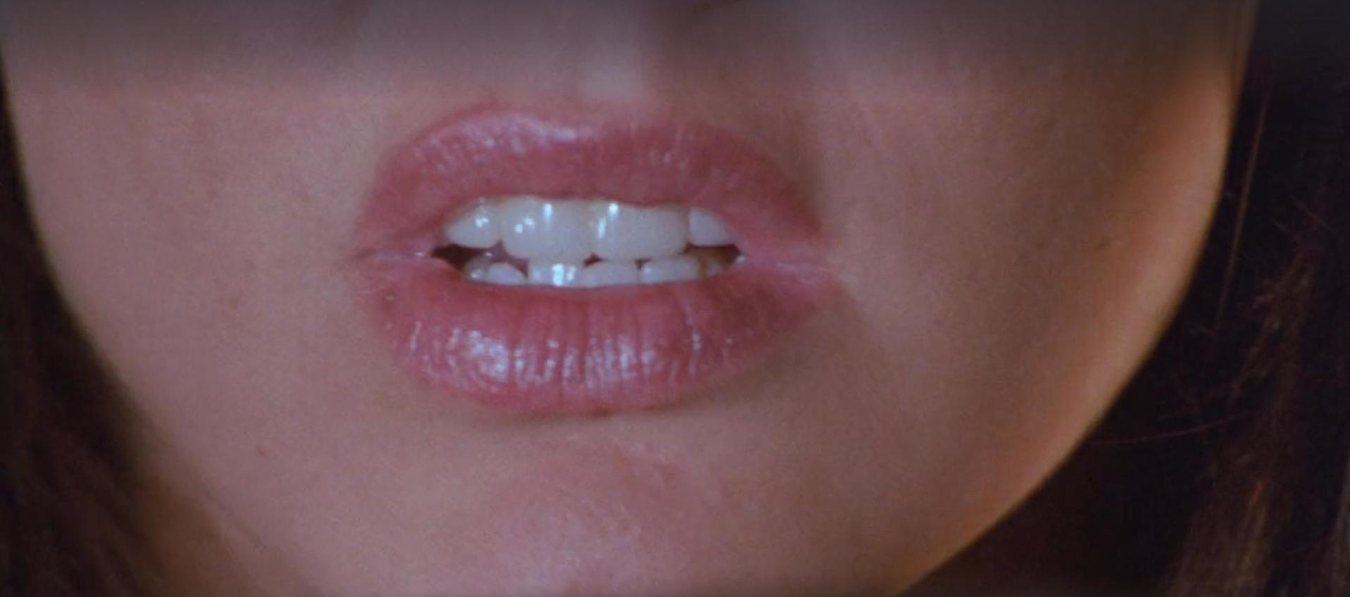 Nahaufnahme von rosafarbenen Lippen mit einem leichten Grinsen und sichtbaren weißen Zähnen.