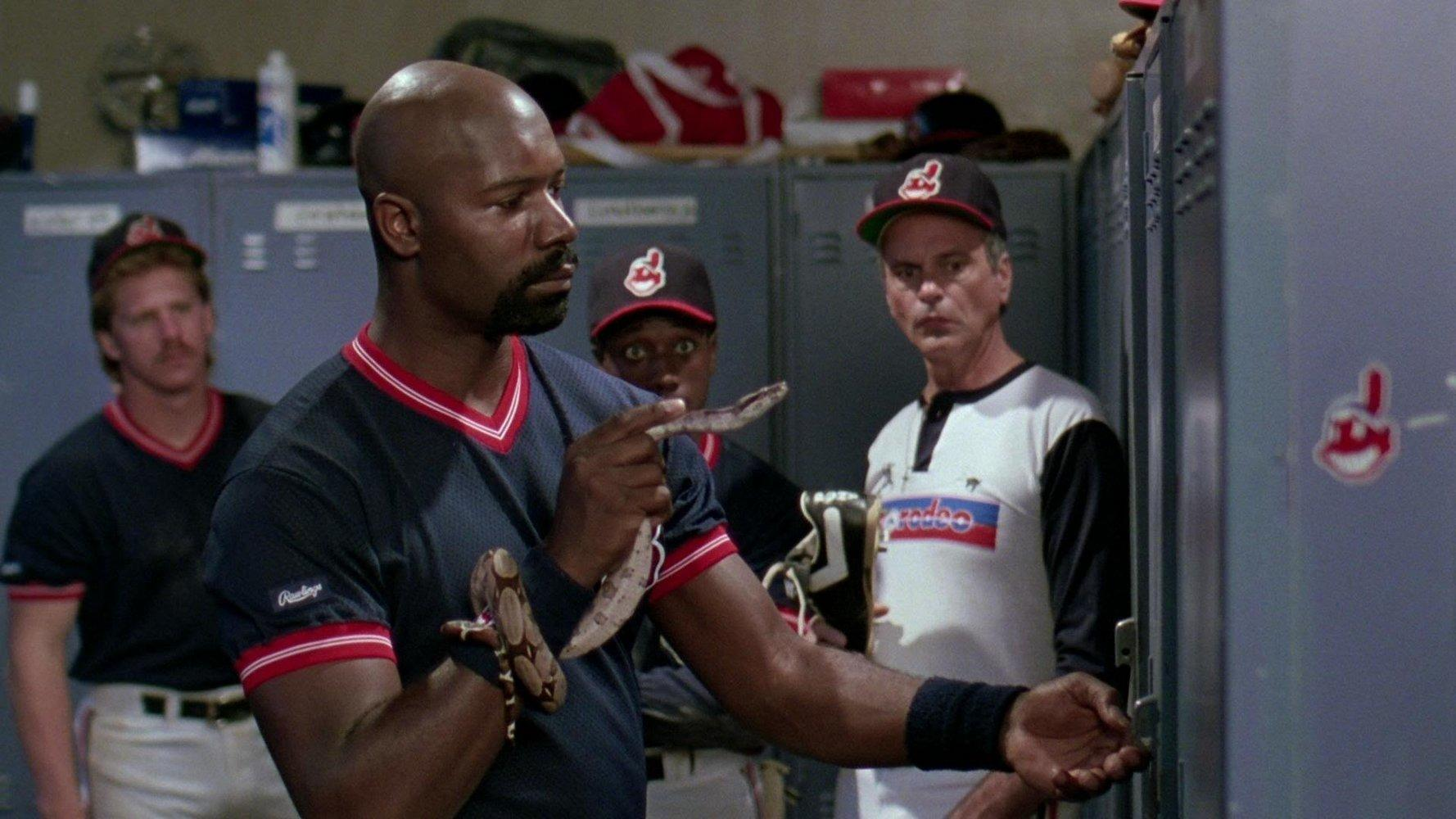 Ein Baseballspieler hält eine Schlange. Andere Spieler stehen im Hintergrund.