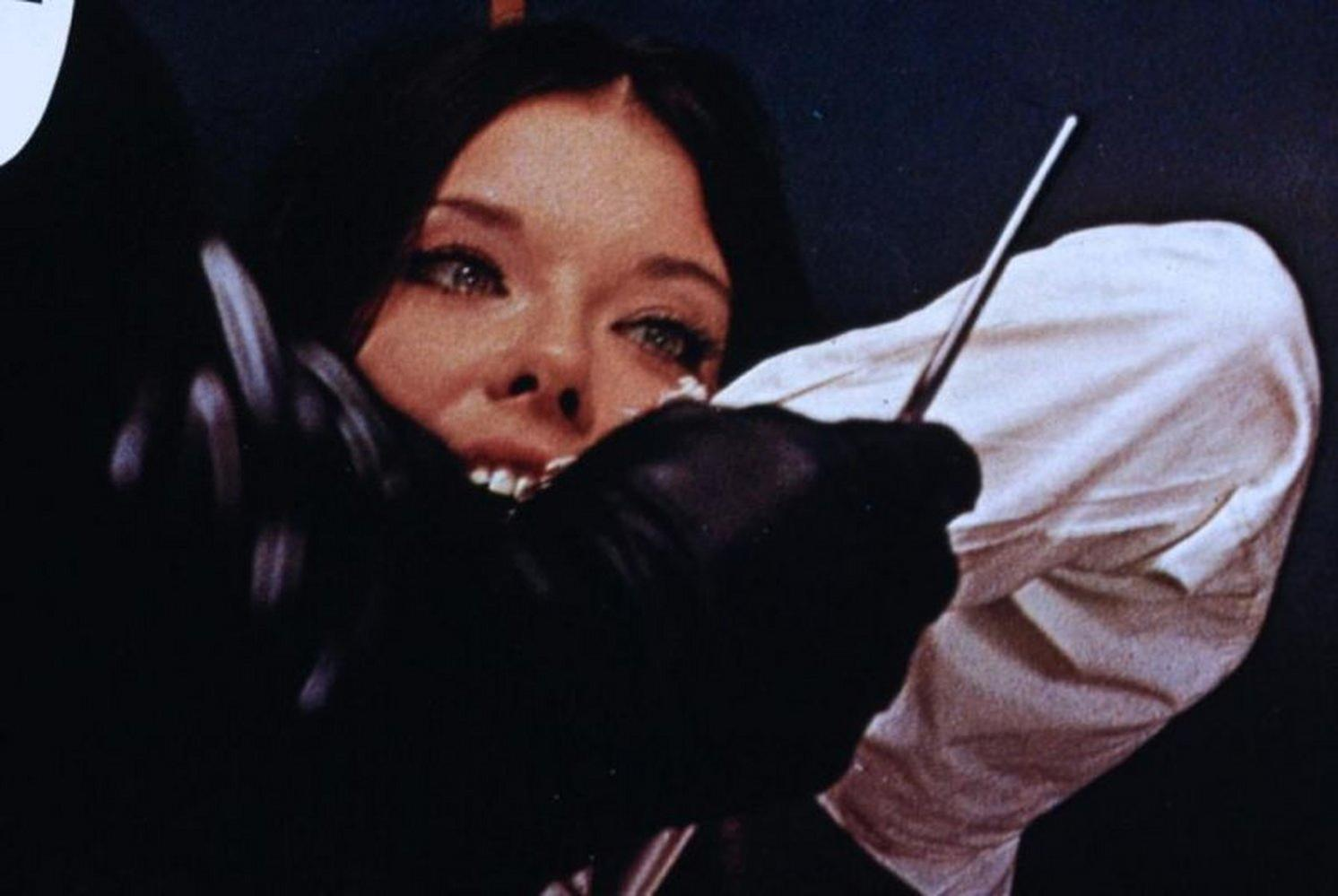 Eine Frau mit weit aufgerissenen Augen wird von einer Hand in Schwarz festgehalten.