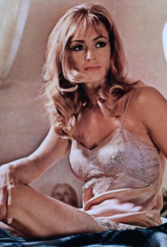 Eine Frau mit blonden Haaren sitzt auf einem Bett und trägt ein Spitzen-Camisole.