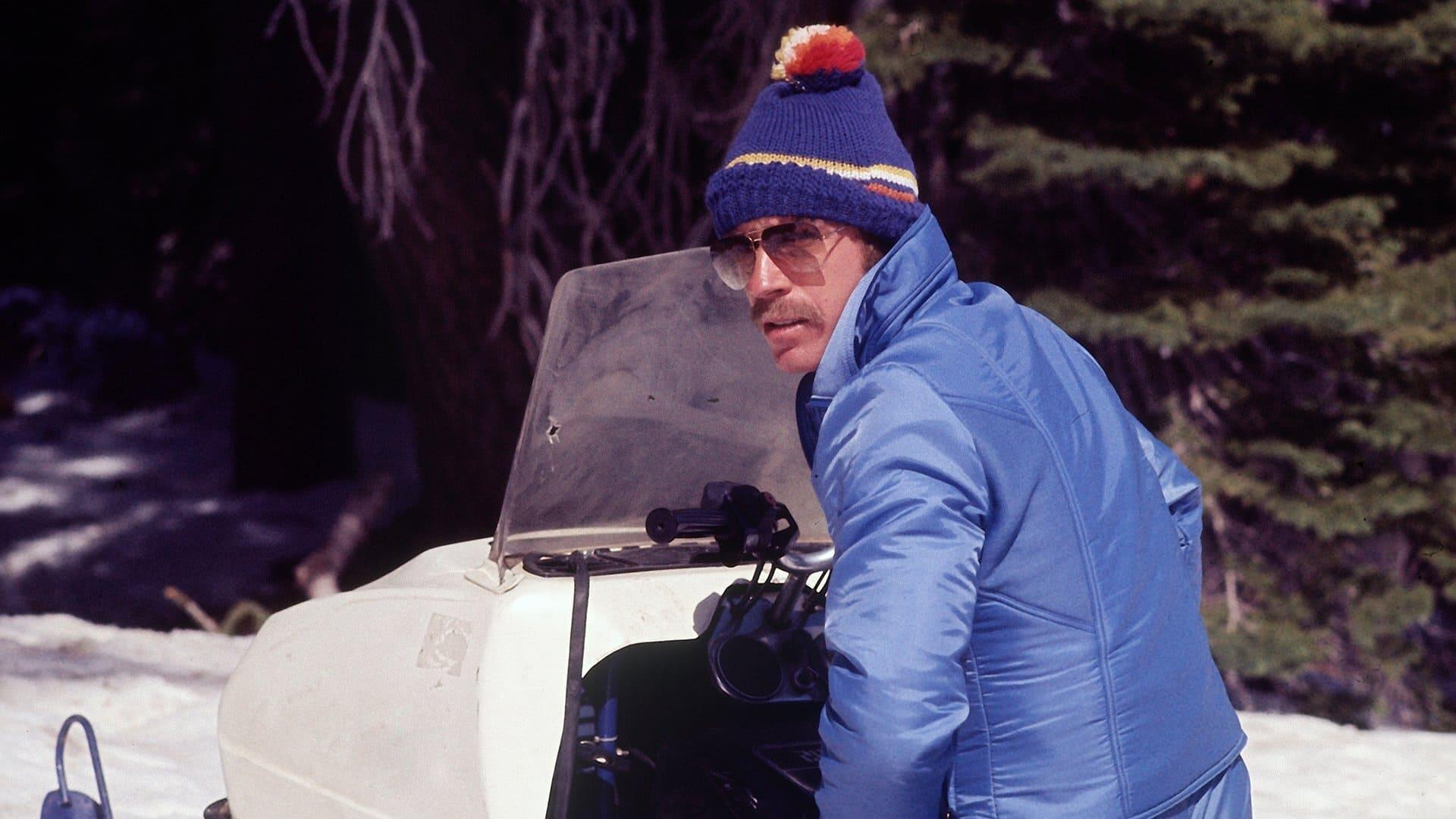 Mann in blauer Jacke und Mütze sitzt auf einem Schneemobil im Schnee.