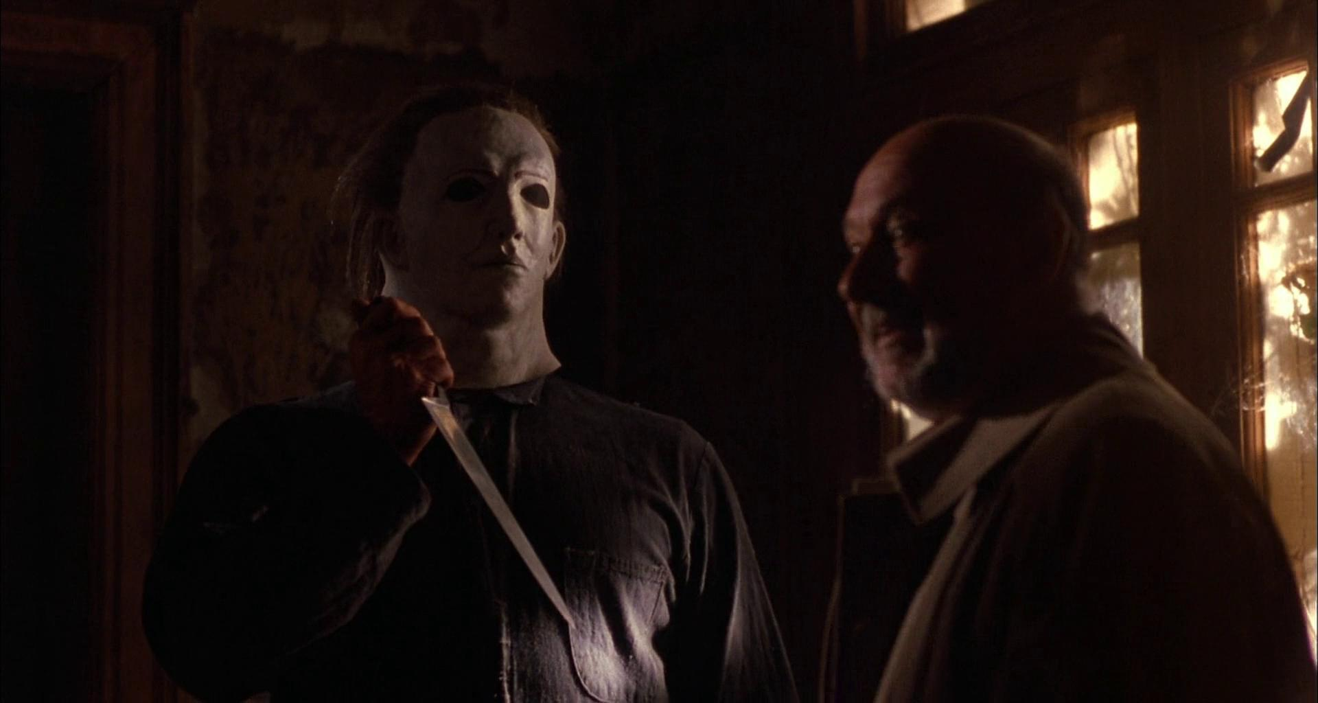 Mann mit Maske und Messer spricht mit einem Mann mit Bart.