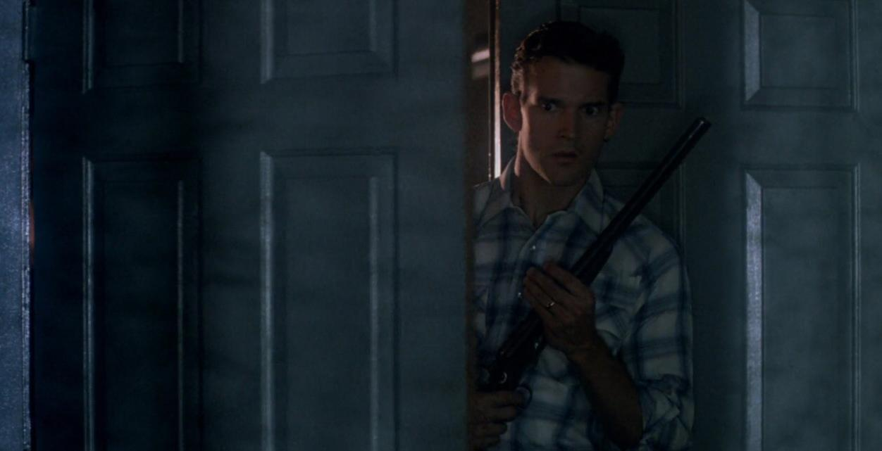 Mann mit Gewehr späht durch eine Tür.