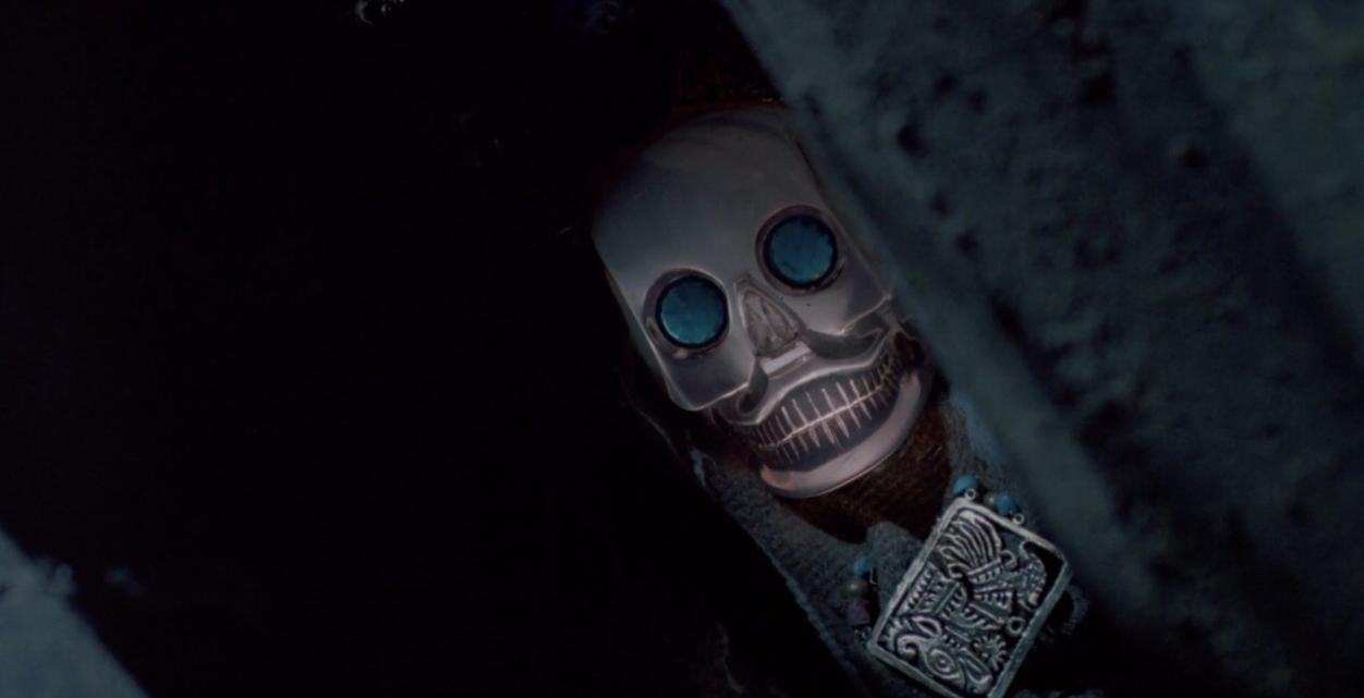 Ein silberner Totenkopf mit blauen Augen liegt auf Stoff. Ein Anhänger ist sichtbar.