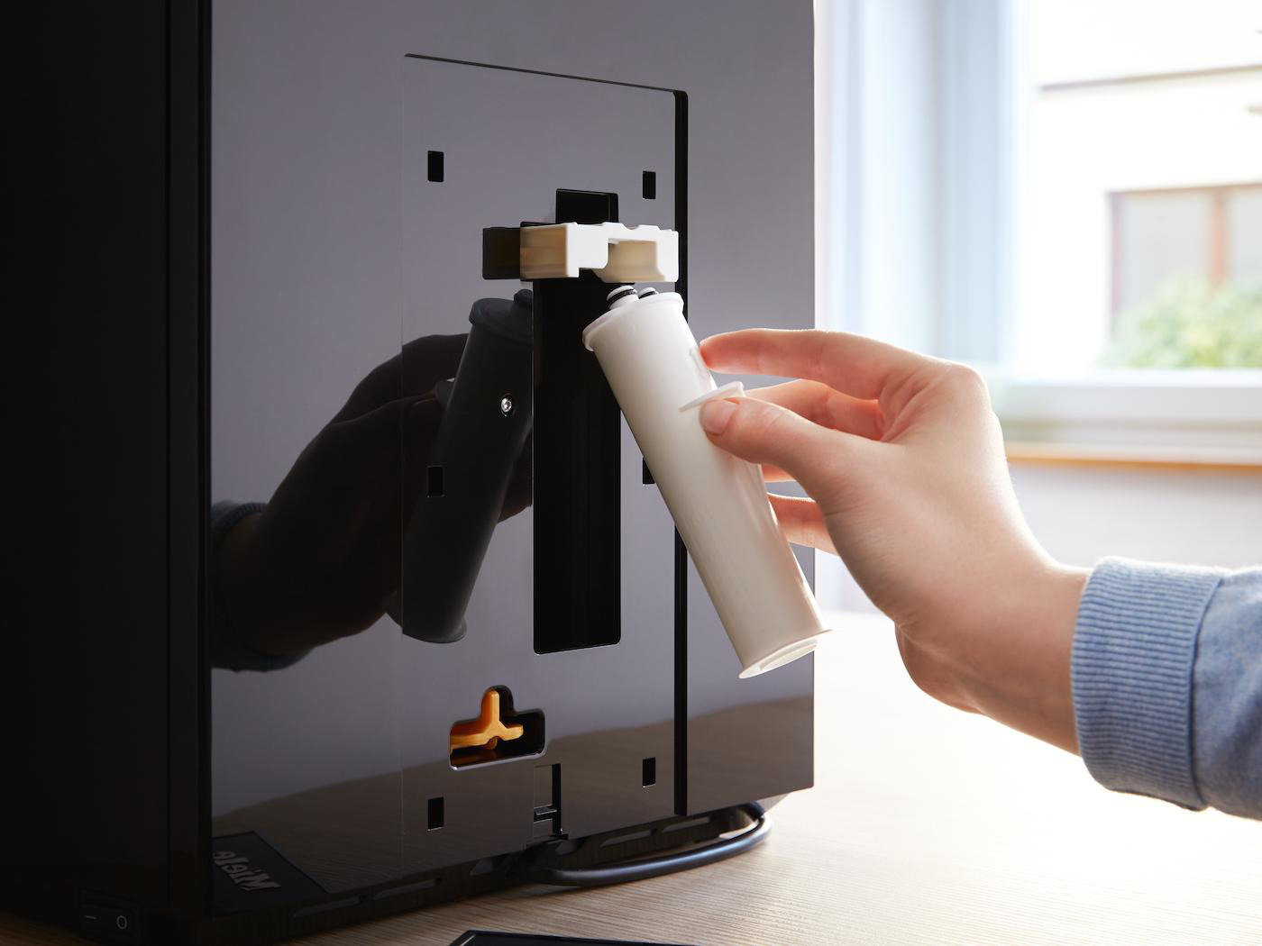 Hand setzt weißen Wasserfilter in schwarze Kaffeemaschine ein.