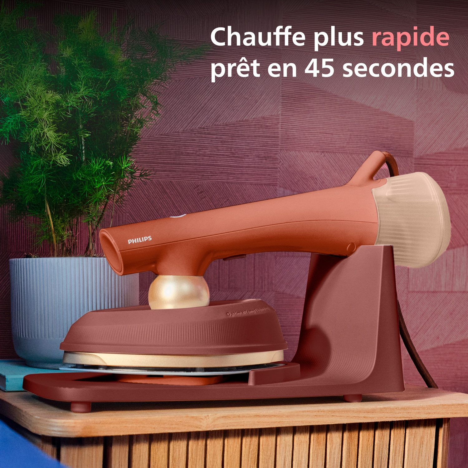 Un support de fer à vapeur corail avec fer et plante sur table en bois.