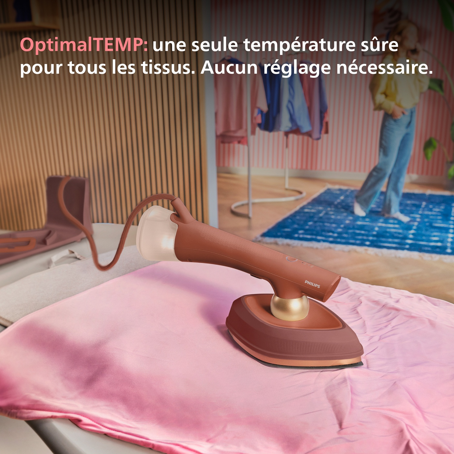 Un fer à vapeur Philips marron sur tissu rose, avec planche à repasser au fond.
