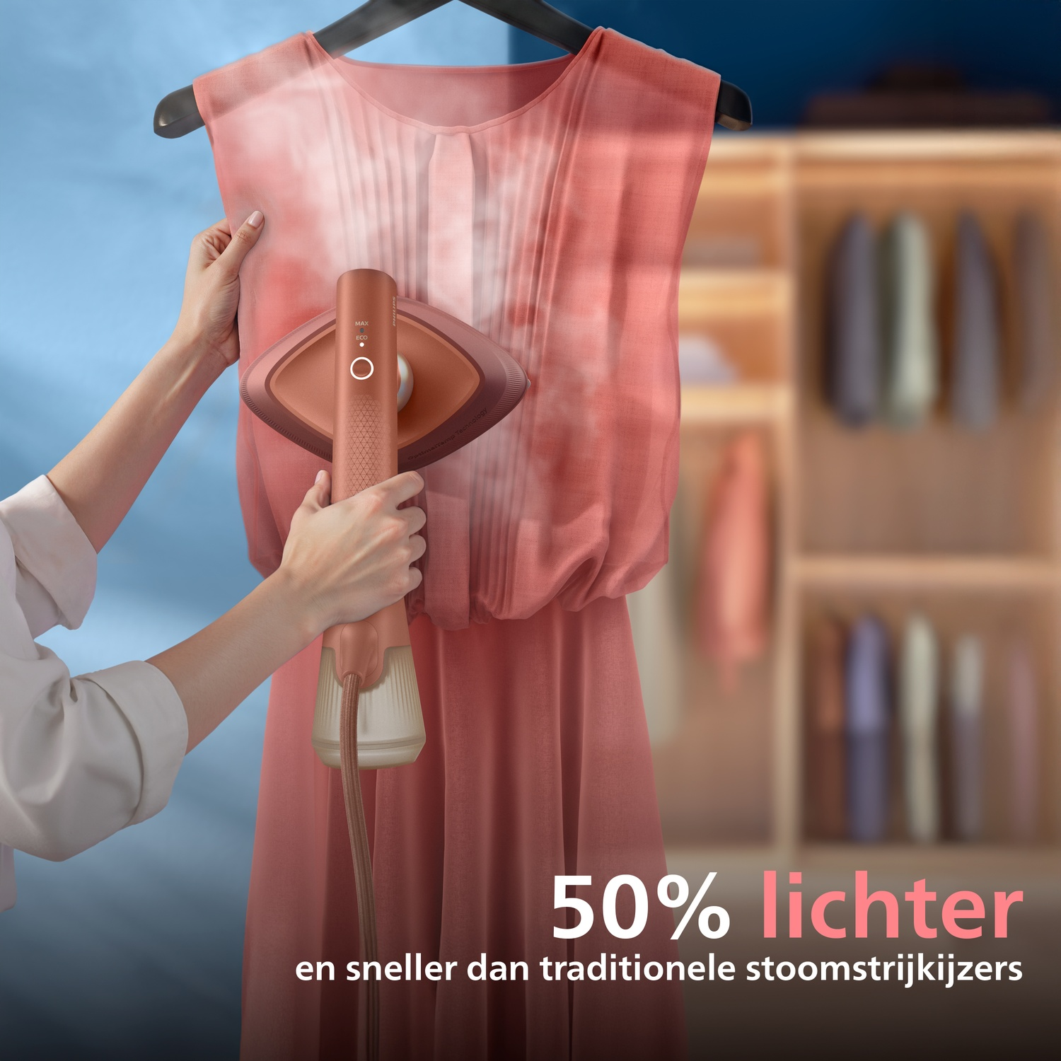Hand holds garment steamer smoothing a pink dress. Wardrobe in background.