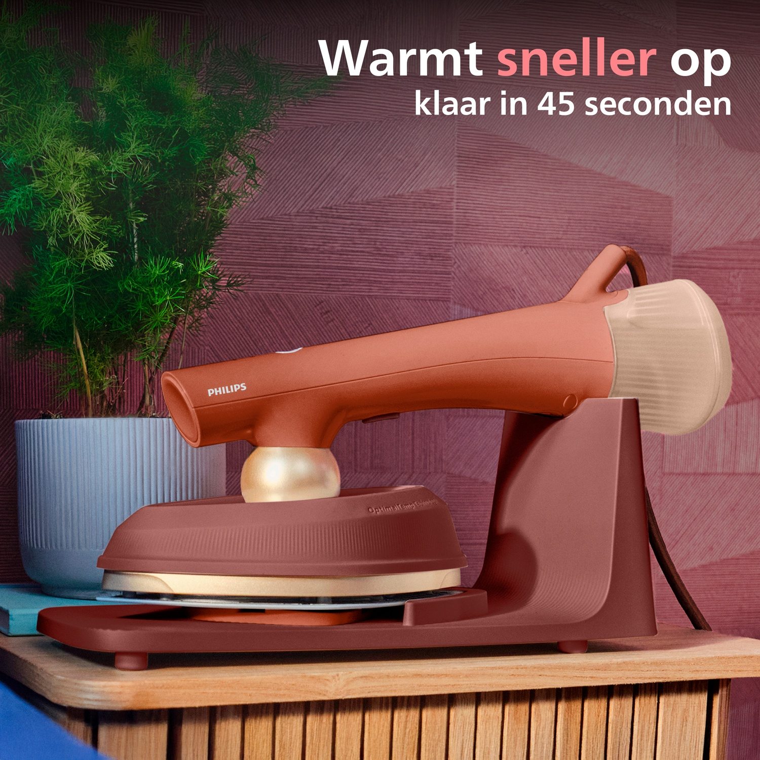 A coral-colored garment steamer sits on a wooden shelf next to a plant.