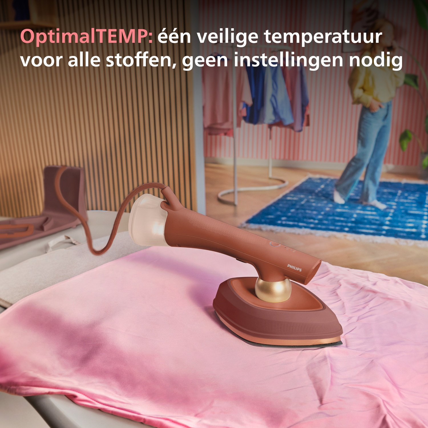 A steam iron on pink fabric. Clothes on a rack in the background.