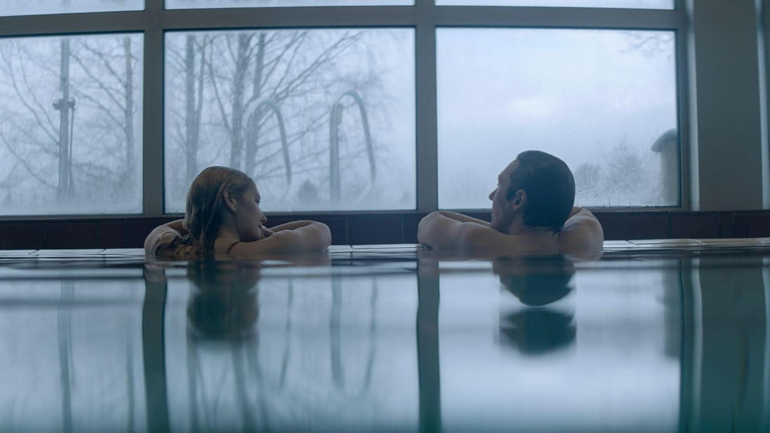 Zwei Personen im Pool vor einem großen Fenster mit Bäumen im Freien.