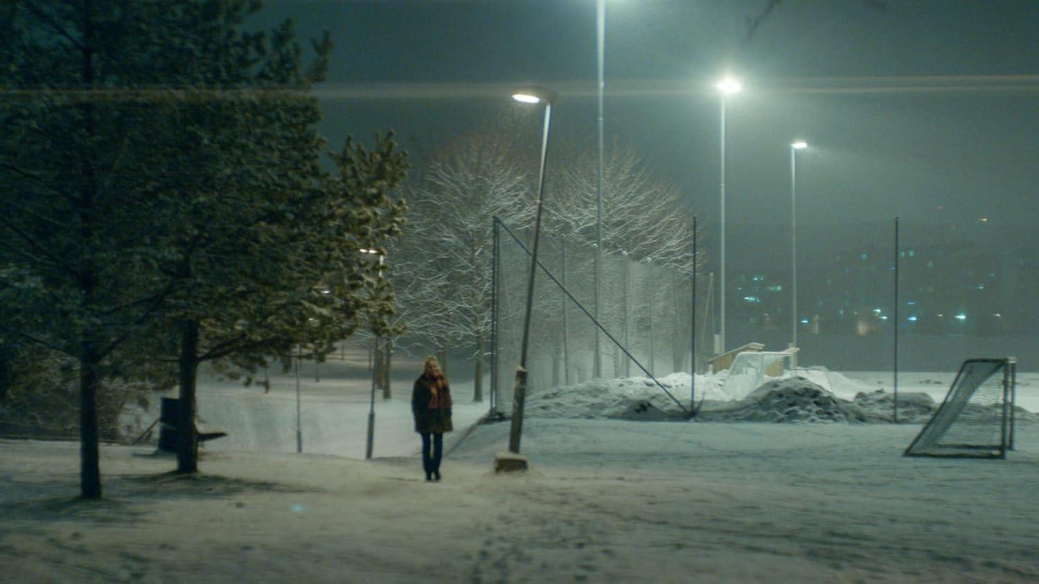 Eine Frau geht durch eine verschneite Landschaft bei Nacht, beleuchtet von Laternen.