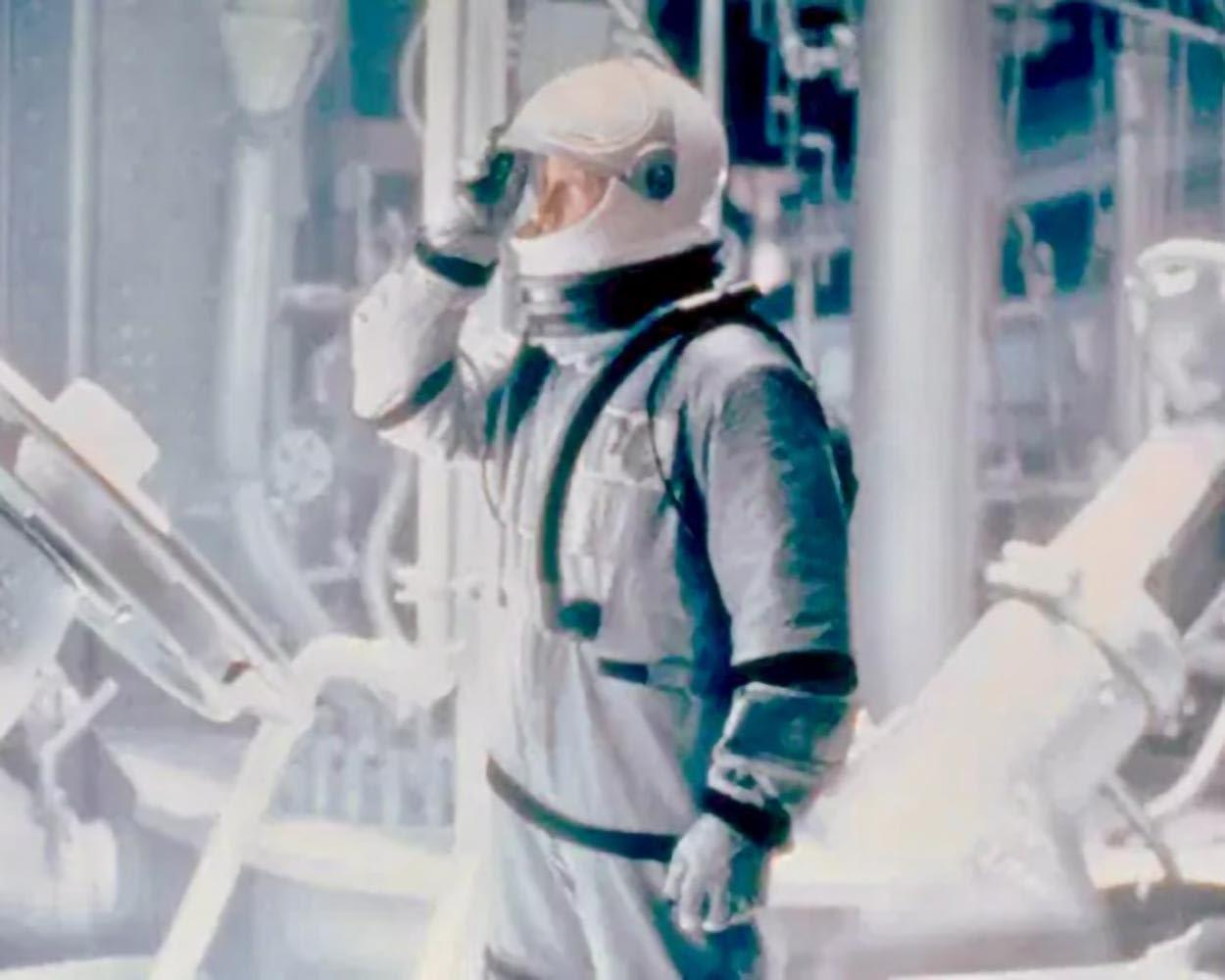 Ein Astronaut in einem weißen Anzug steht in einer Fabrik und blickt nach links.
