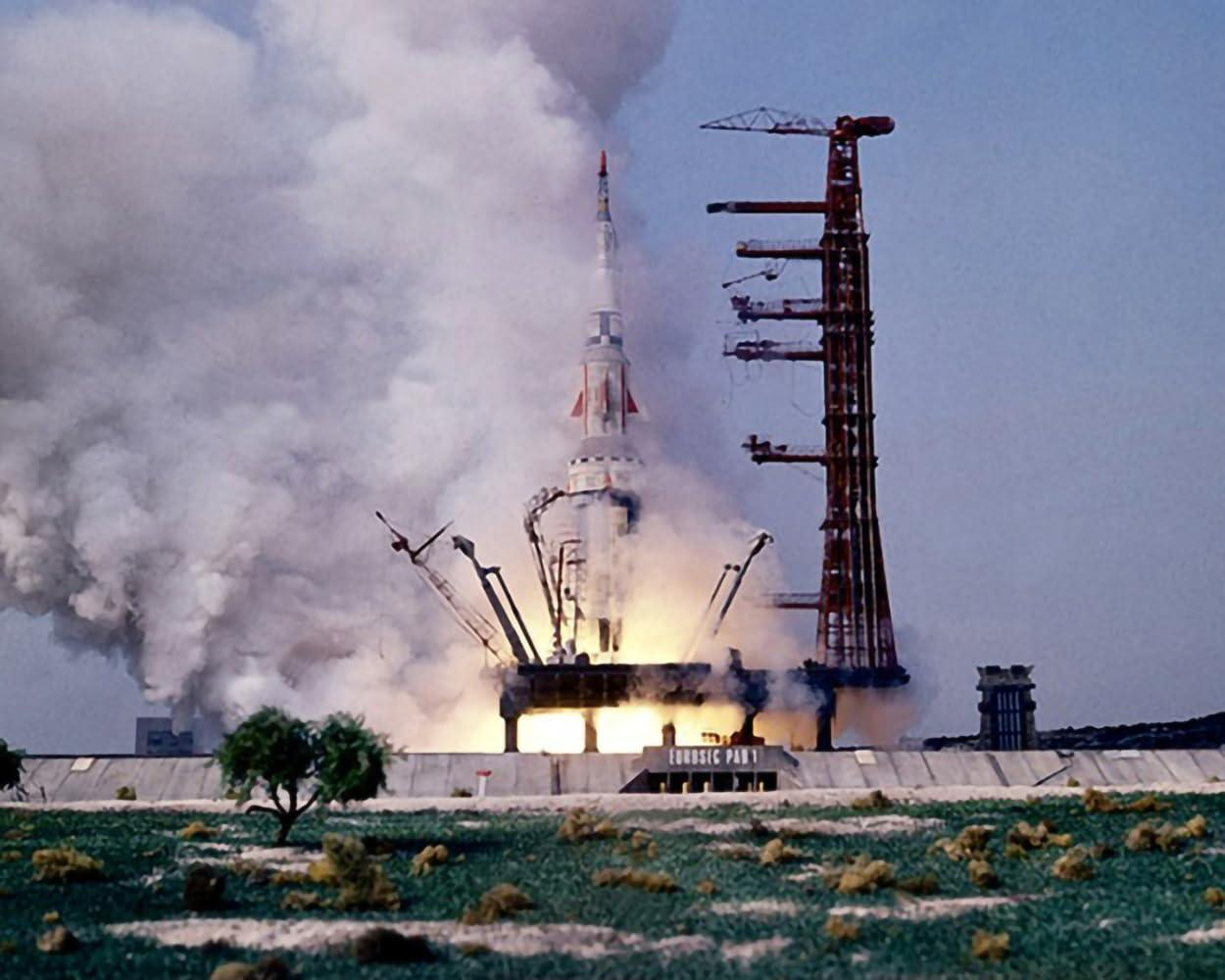 Eine Rakete startet mit viel Rauch und Flammen. Ein roter Turm steht daneben.