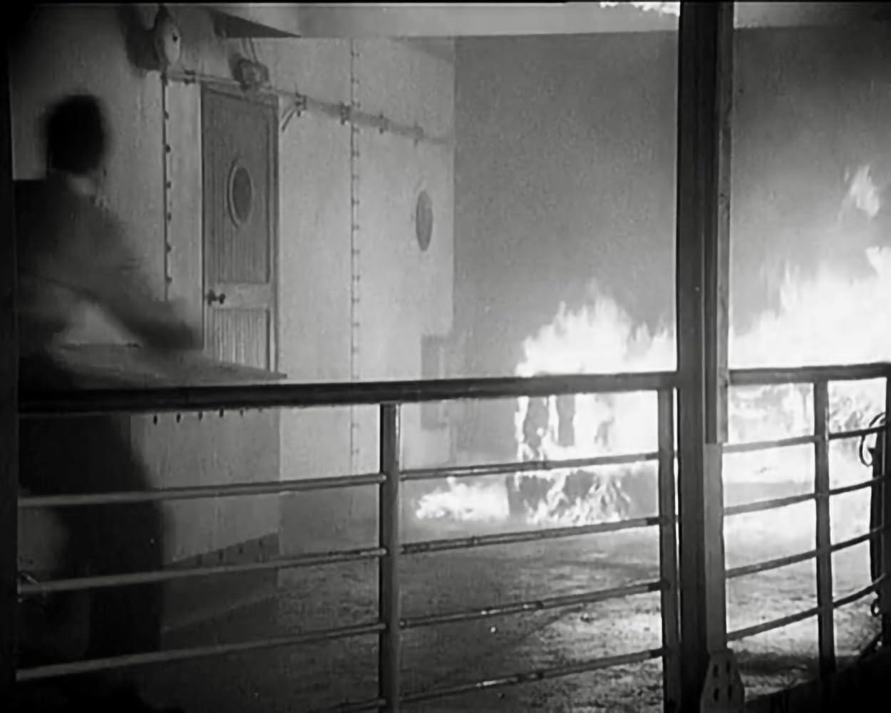 Ein Mann blickt auf ein brennendes Schiff. Flammen lodern hell auf.