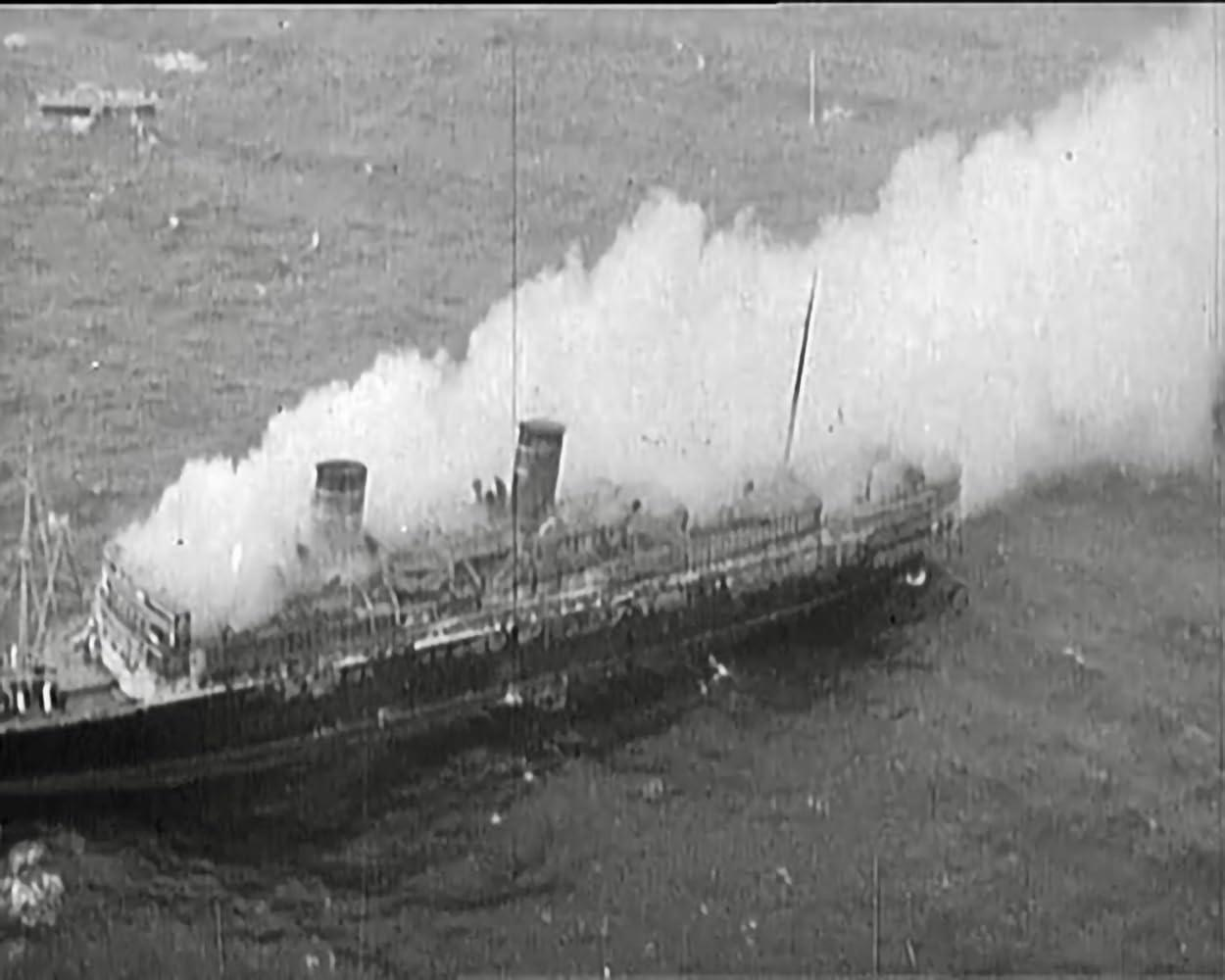 Ein brennendes Schiff mit viel Rauch auf dem Meer.