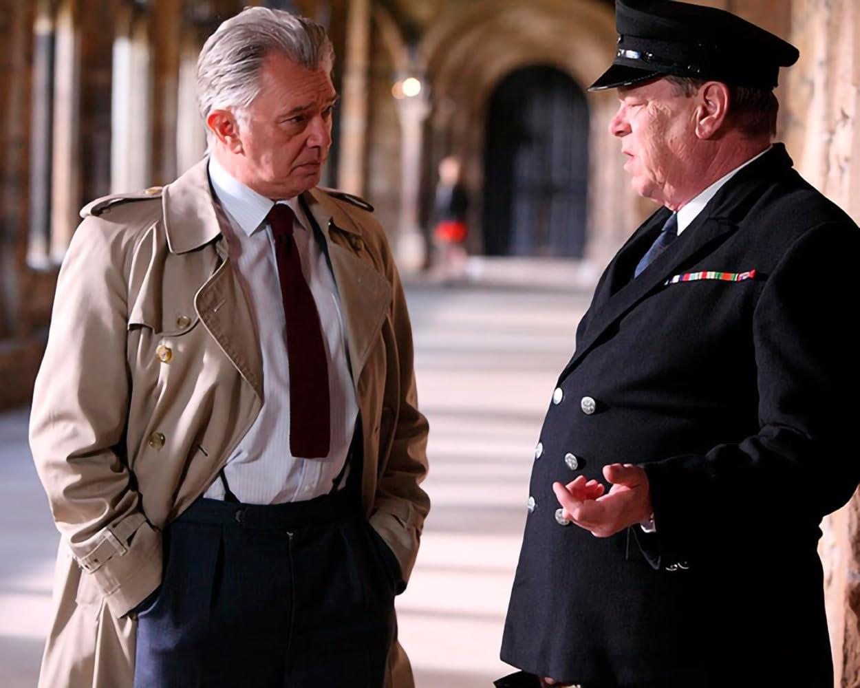 Zwei Männer unterhalten sich in einem steinernen Gang. Einer trägt einen Trenchcoat, der andere eine Uniform.