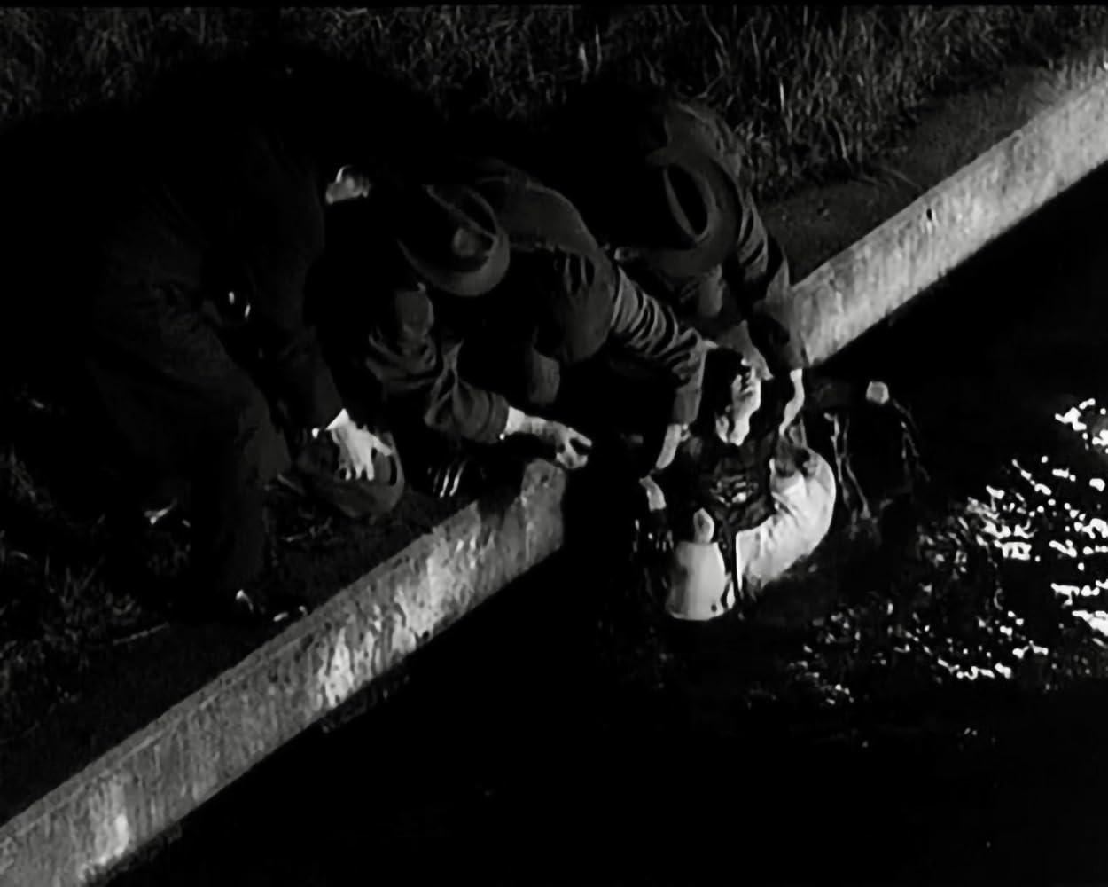 Männer in Hüten ziehen eine Person aus dem dunklen Wasser zu einem Betonufer.
