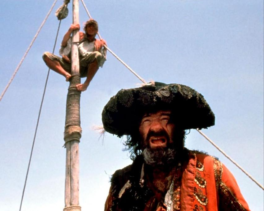 Ein Mann mit Bart und Hut sitzt auf einem Mast, ein Junge klettert darüber.