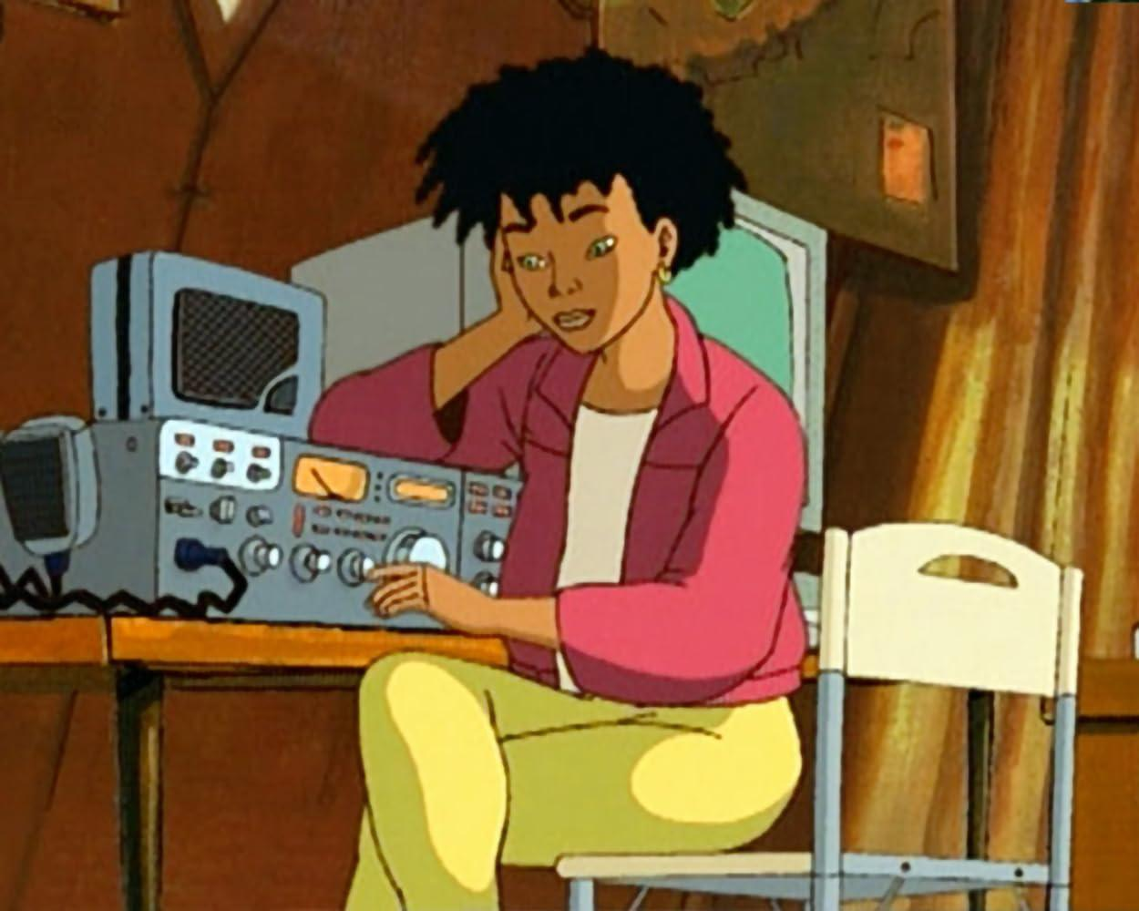 Eine Frau mit Afro-Haaren sitzt an einem Tisch und bedient ein Funkgerät.