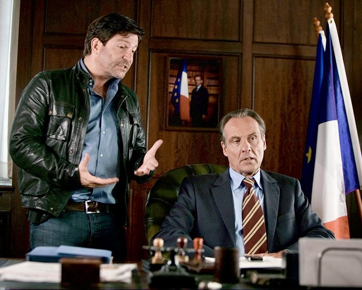 Ein Mann im Lederjacke spricht, ein anderer Mann sitzt am Schreibtisch.