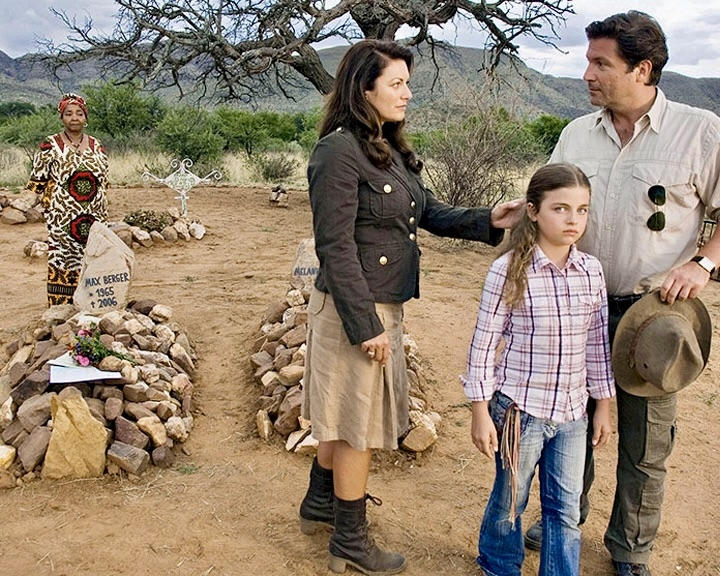 Eine Familie steht auf einem Friedhof. Ein Baum steht im Hintergrund.