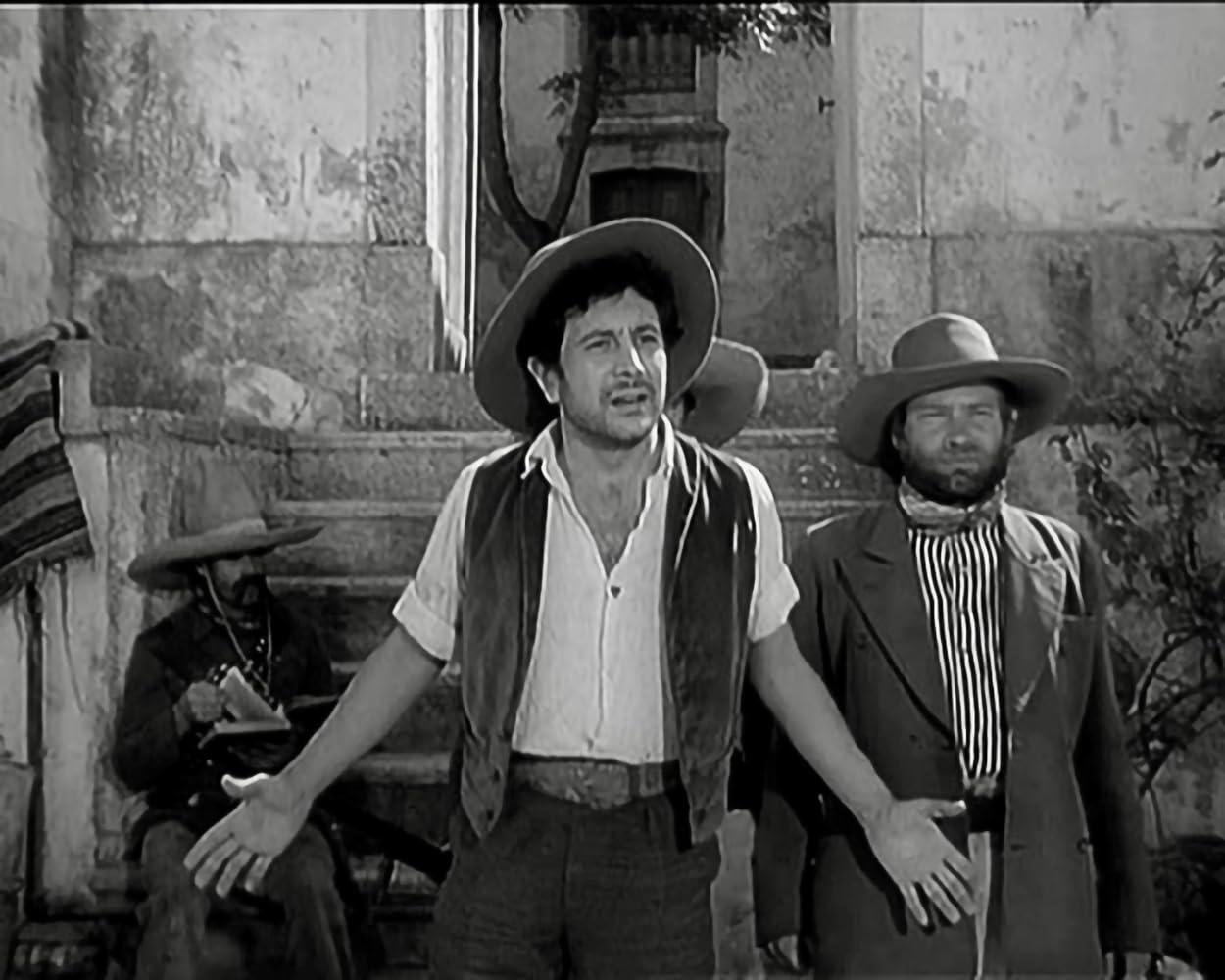 Drei Männer in Cowboykleidung stehen vor einer Steintreppe. Einer spricht.