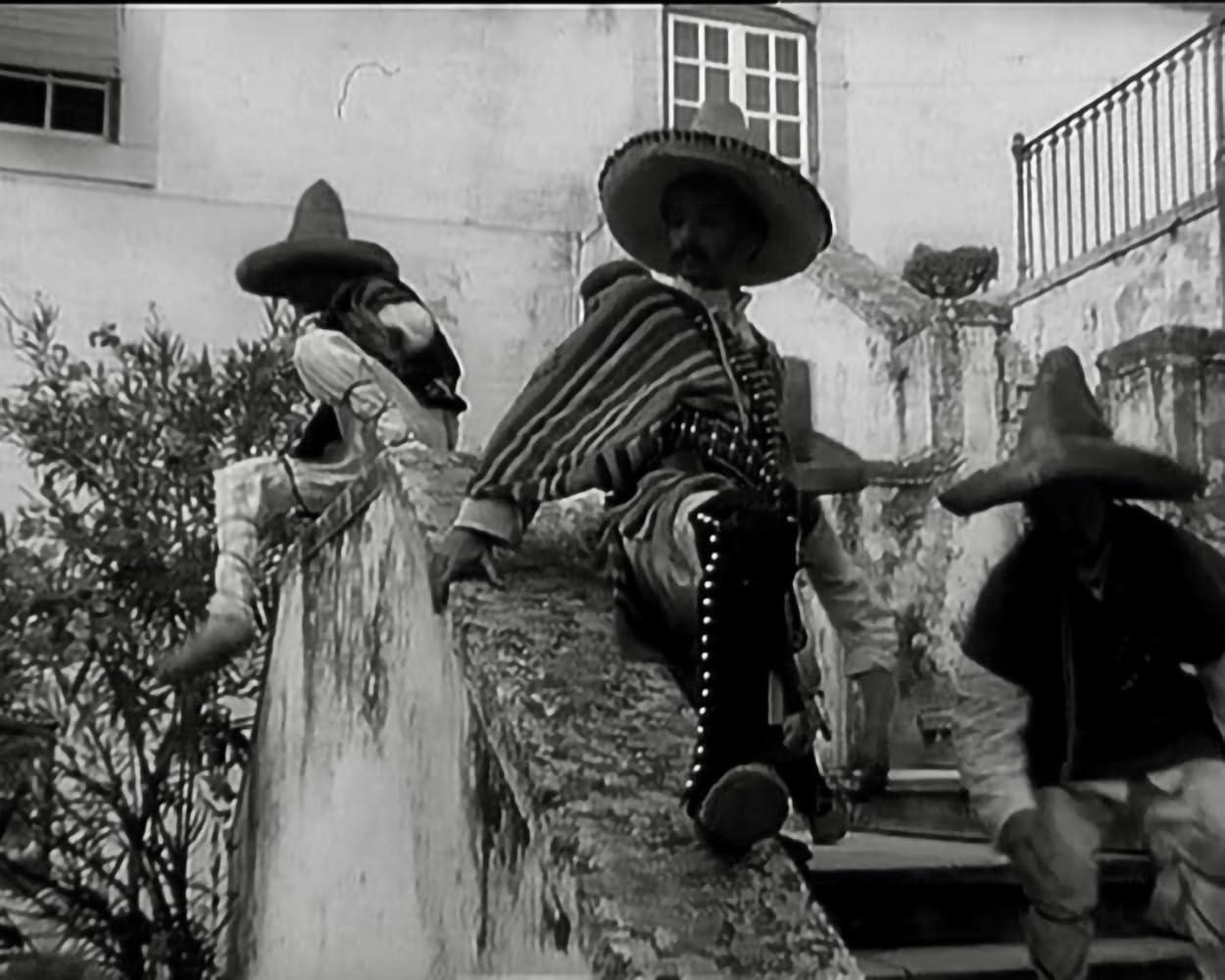 Drei Männer in Sombreros und traditioneller Kleidung sitzen und stehen auf einer Steintreppe.