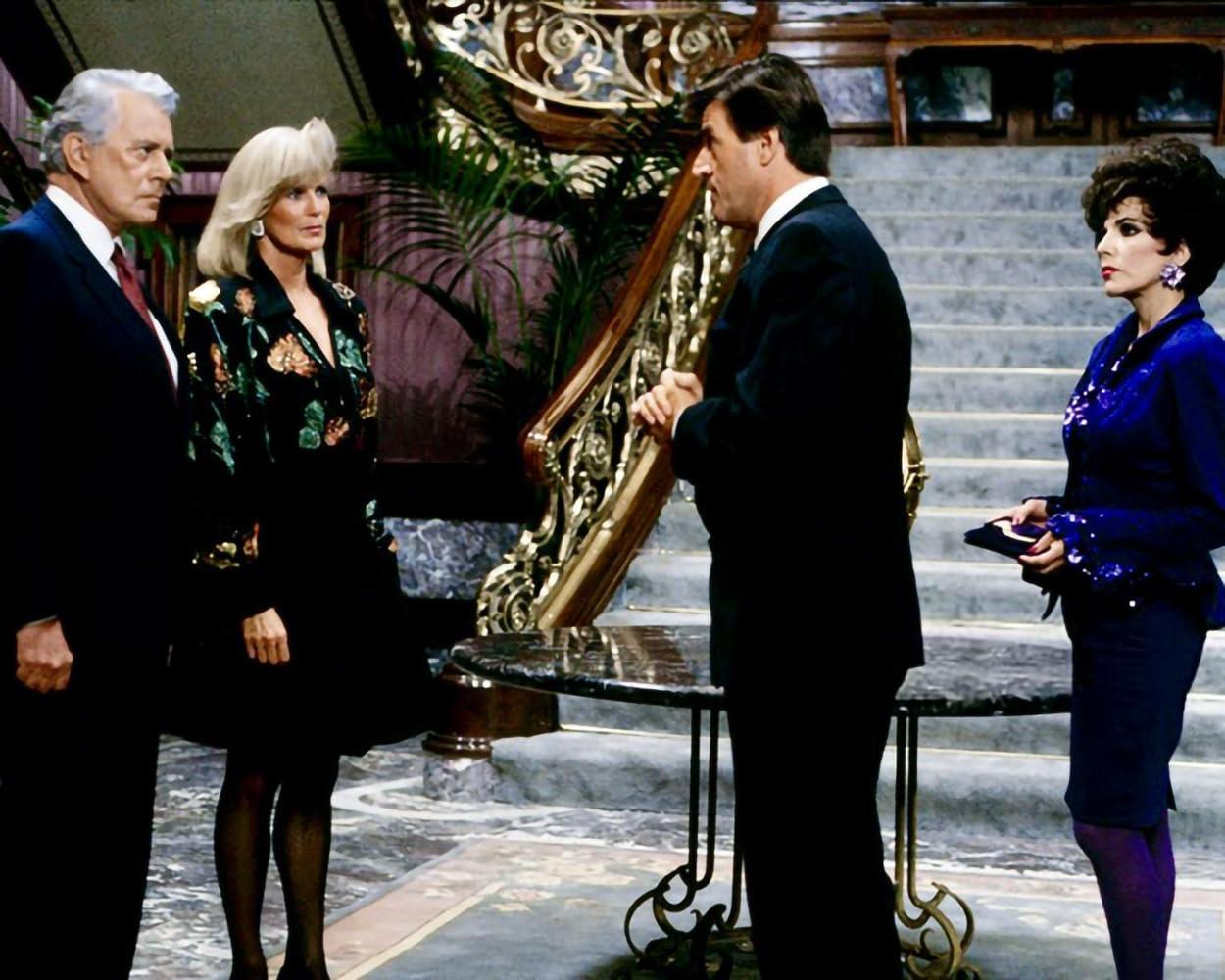 Vier Personen stehen in einem opulenten Foyer mit einer geschwungenen Treppe.
