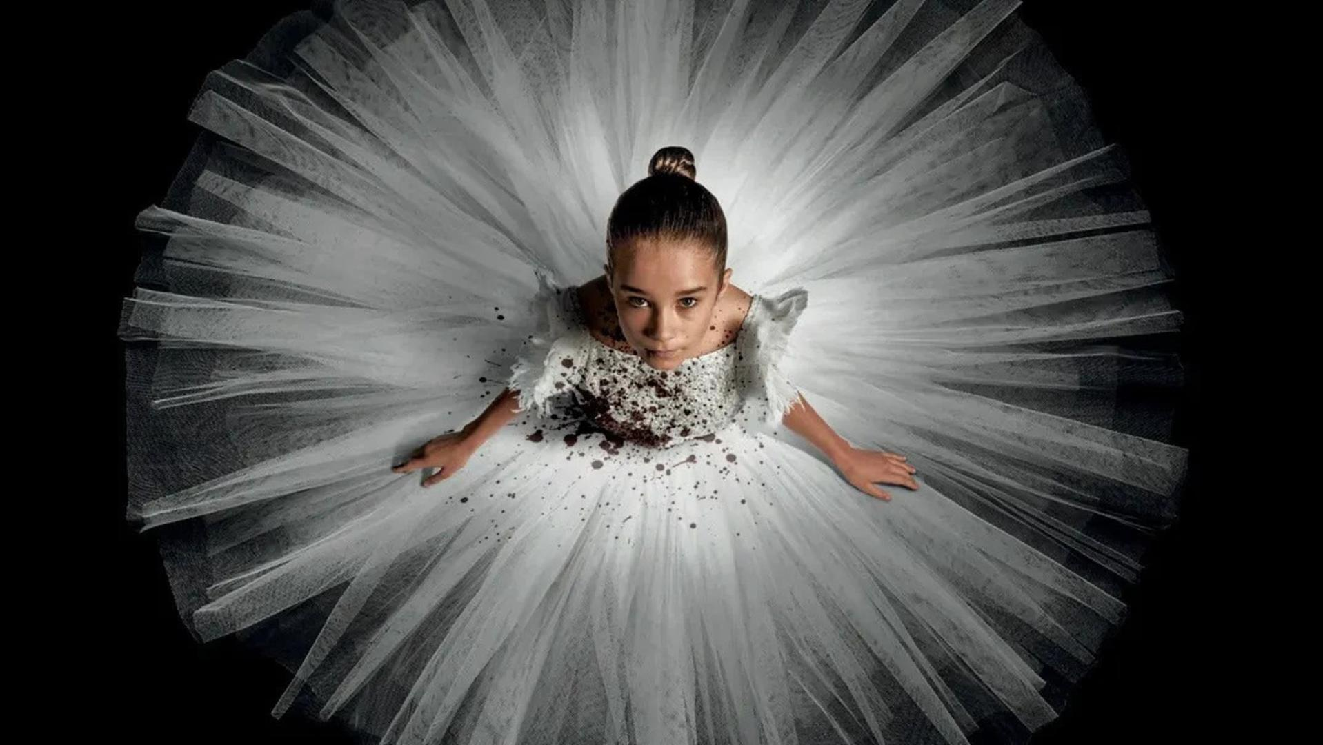 Ein junges Mädchen in einem weißen Tutu mit dunklen Flecken, blickt nach oben.