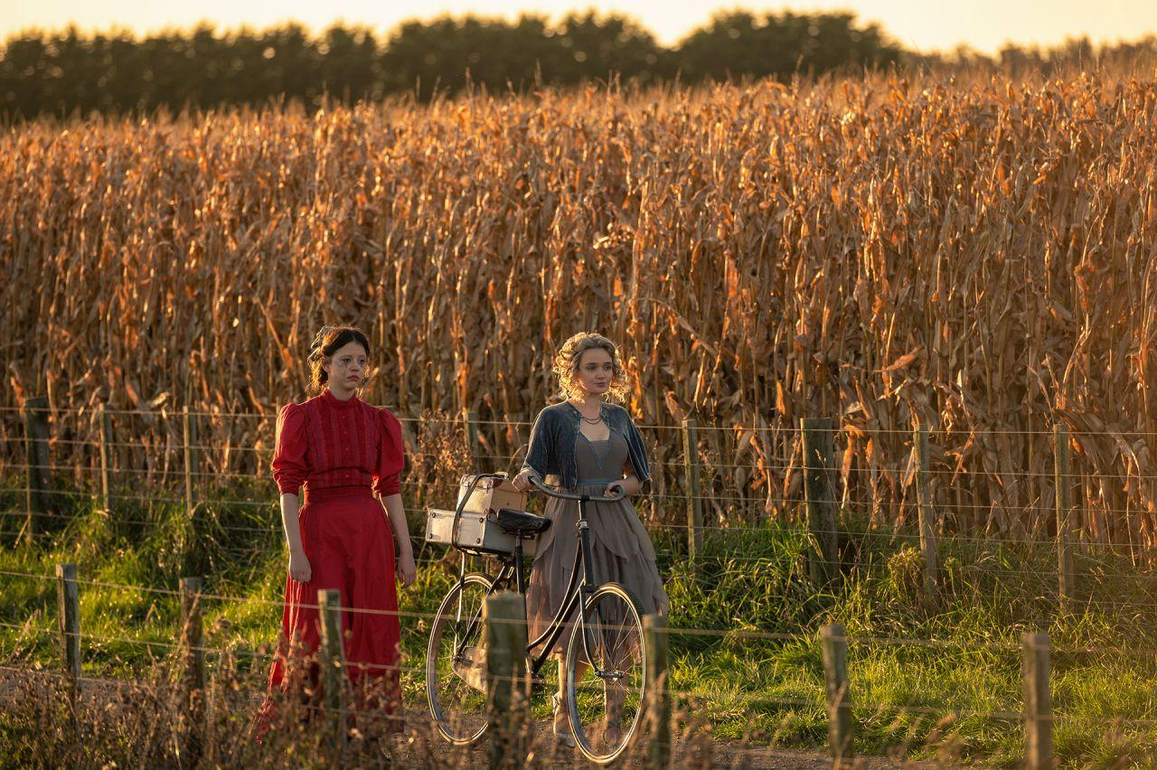 Zwei Frauen stehen neben einem Fahrrad in einem Feld mit trockenem Mais unter Abendlicht.