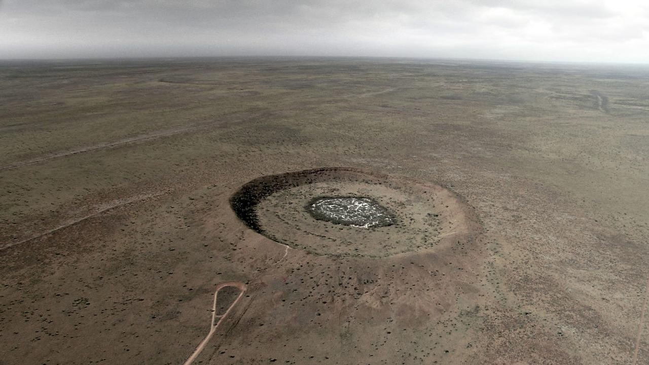 Eine Kraterformation in einer flachen, trockenen Landschaft unter einem bewölkten Himmel.