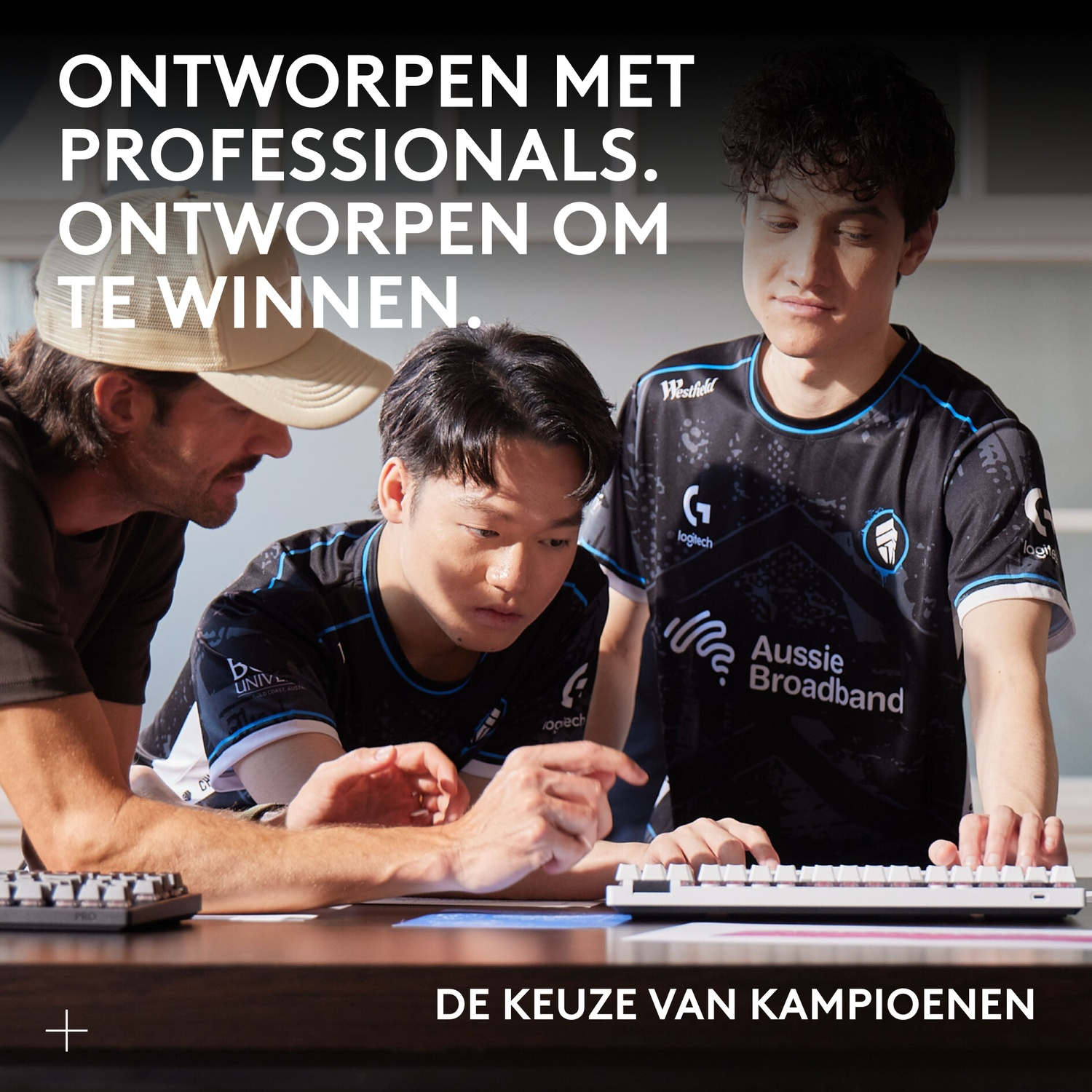 Three men look at a table, two play on keyboards.