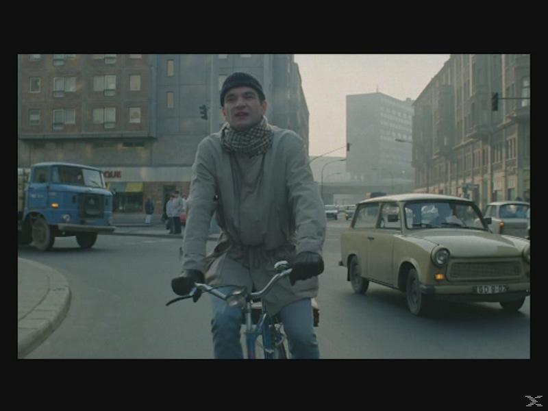 Ein Mann auf einem Fahrrad fährt auf einer Stadtstraße, Autos und Gebäude im Hintergrund.