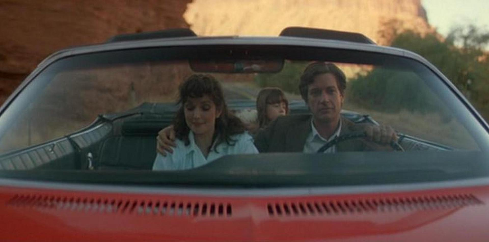 Familie in einem roten Cabrio auf einer Straße mit Wüstenlandschaft.