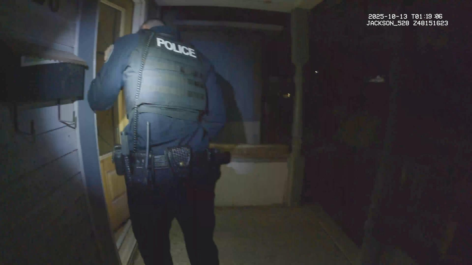 Polizist in Weste und Uniform steht vor einer Tür bei Nacht.