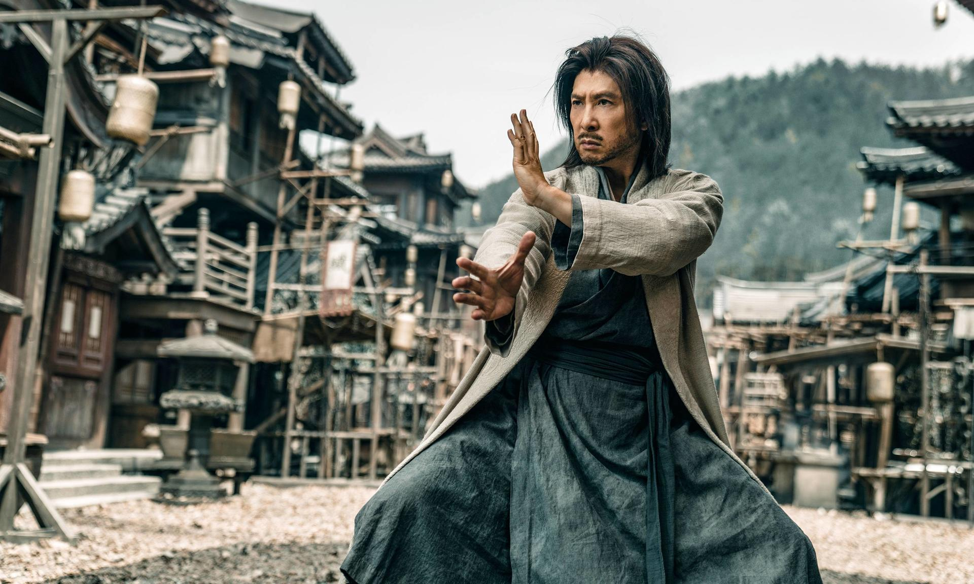 Ein Mann in traditioneller Kleidung übt Kung-Fu vor alten Gebäuden.