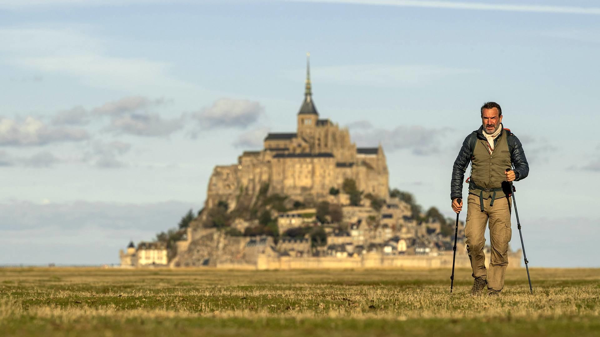 Ein Mann wandert mit Stöcken auf einem Feld zum Mont Saint-Michel.