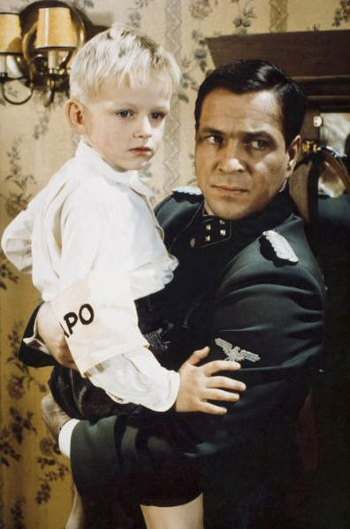 Mann in Uniform hält blonden Jungen mit "IPO"-Armbinde.