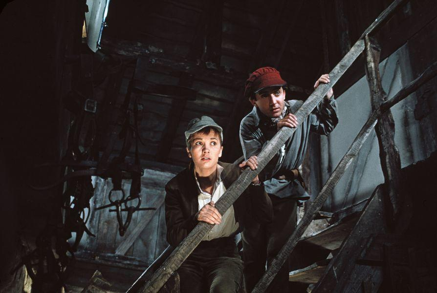 Zwei junge Leute klettern eine Holztreppe in einem dunklen Gebäude hinauf.