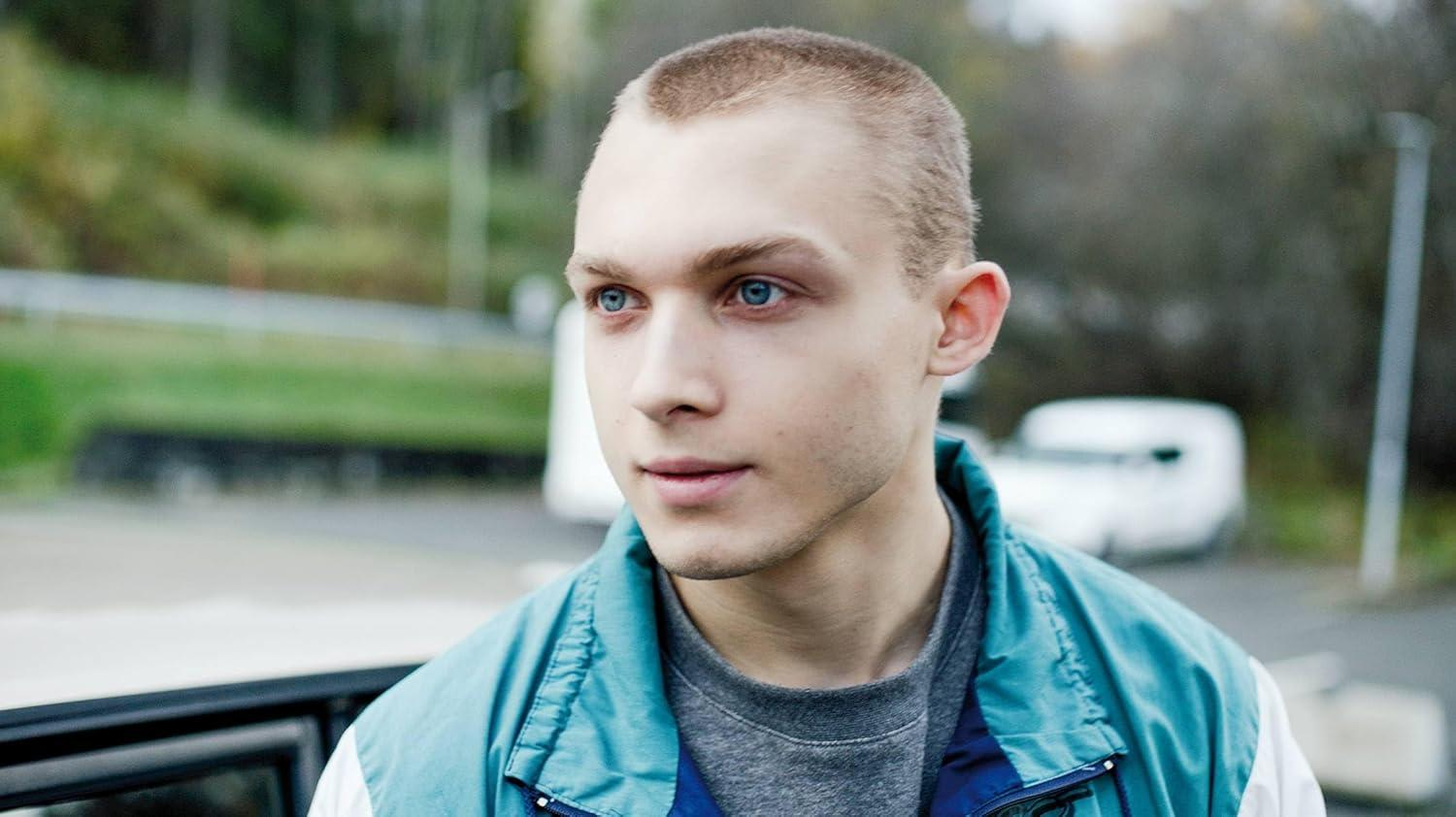 Ein junger Mann mit blauen Augen und kurzgeschorenen Haaren trägt eine blaue Jacke.