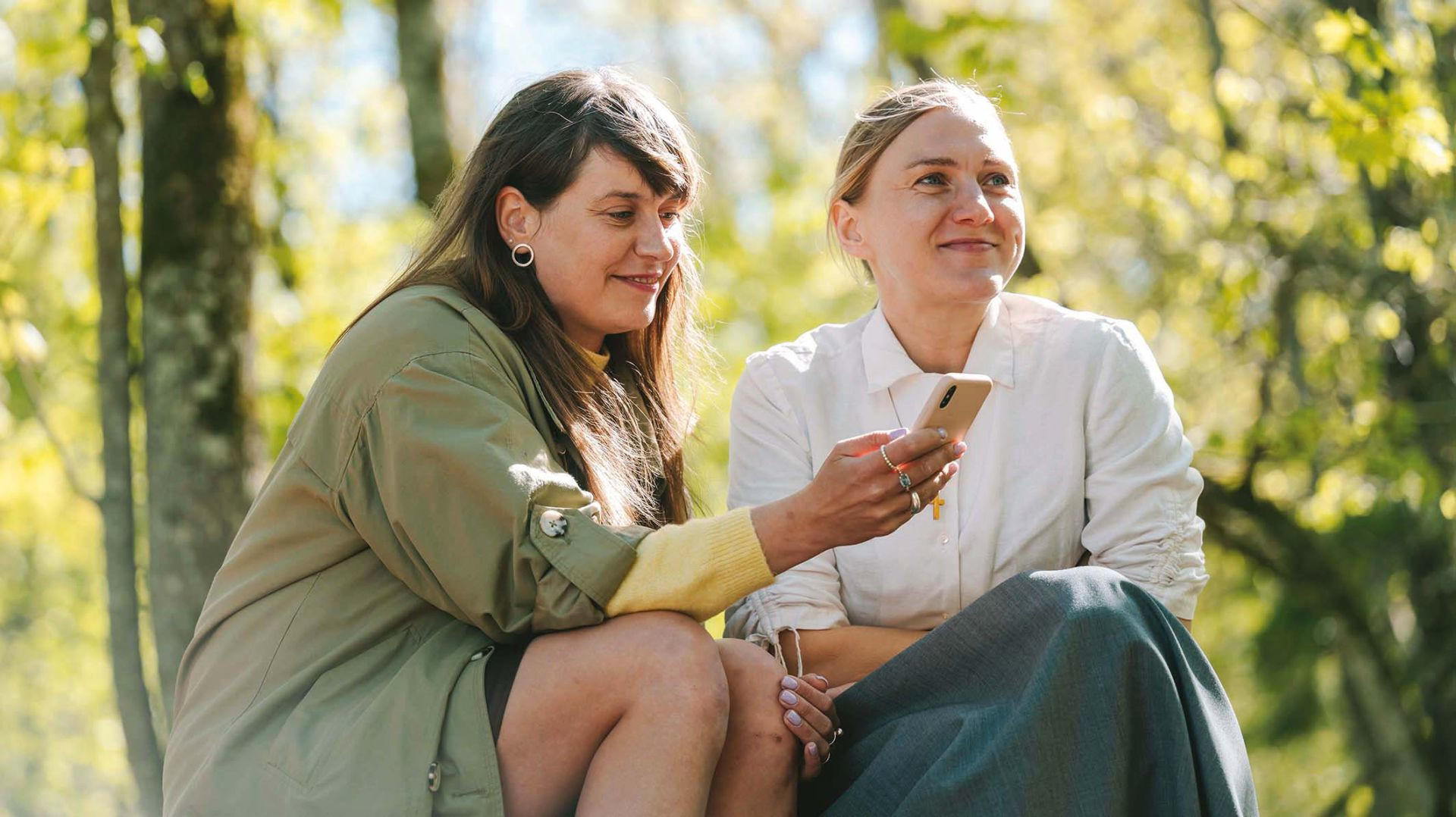 Zwei Frauen sitzen im Freien und betrachten ein Smartphone in der Hand einer Frau.