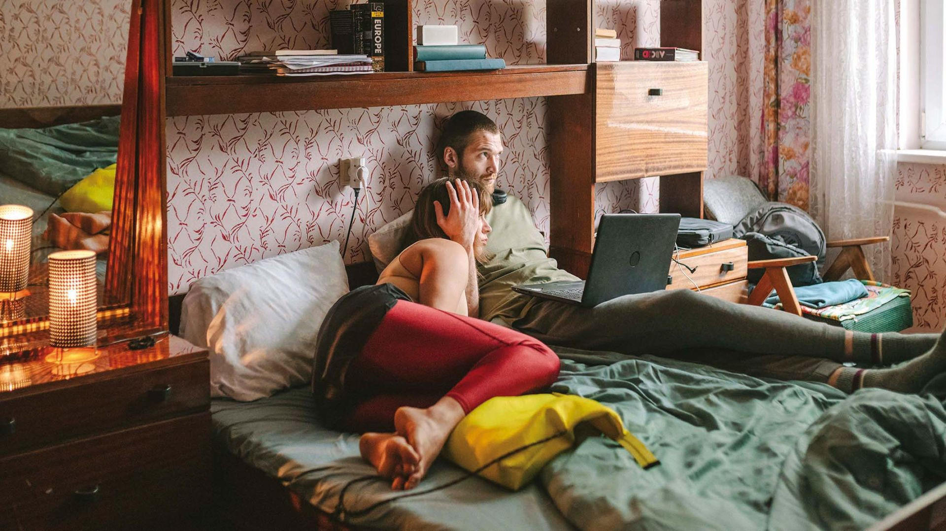 Ein Mann und eine Frau liegen im Bett, sie schauen auf einen Laptop.