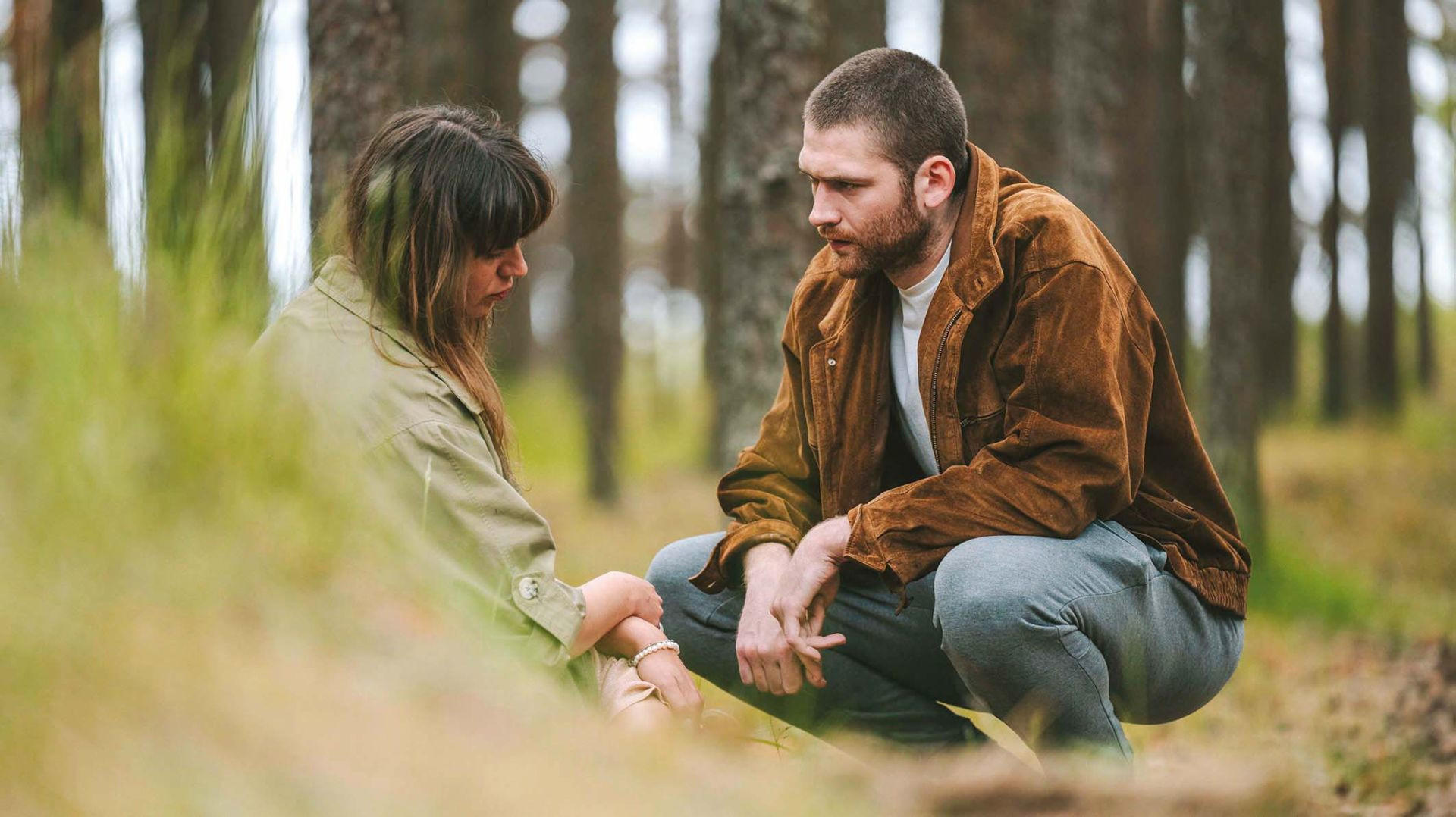 Ein Mann in brauner Jacke und eine Frau in grüner Jacke sitzen im Wald.