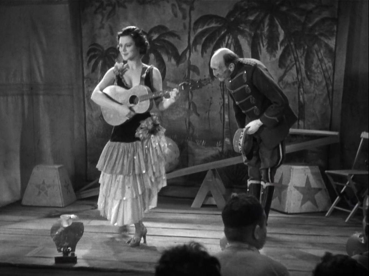 Eine Frau mit Gitarre und ein Mann in Uniform auf einer Bühne.