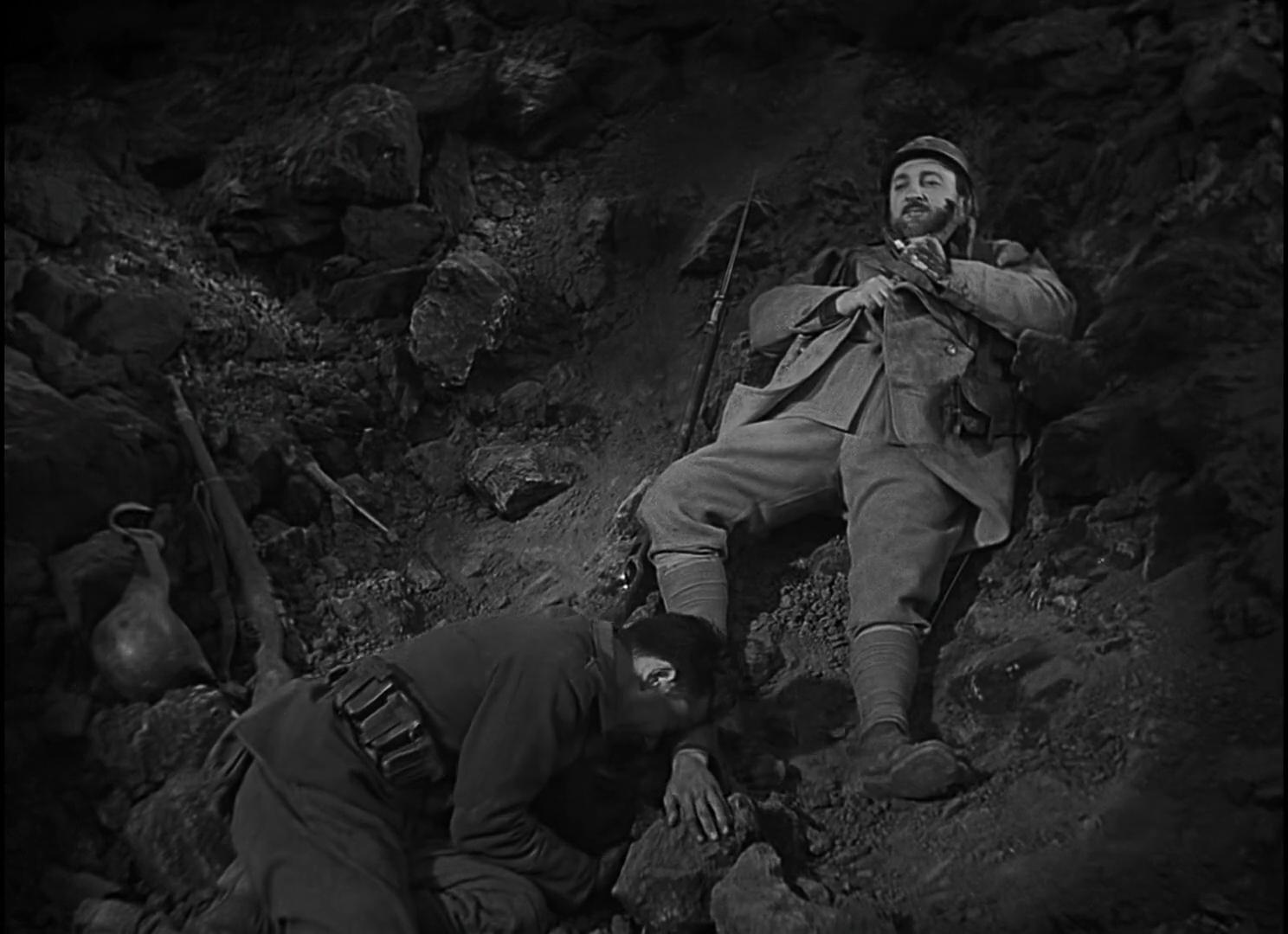 Zwei Soldaten in Uniform in einem felsigen Graben. Einer sitzt, der andere kauert.
