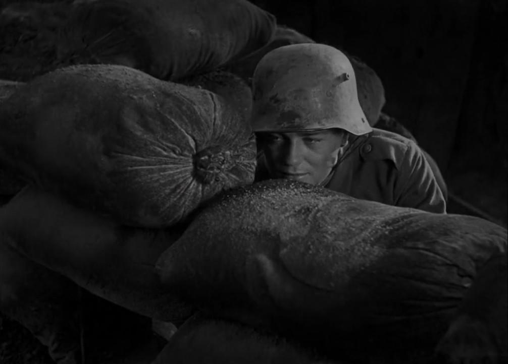 Soldat mit Helm hinter Sandsäcken, Schwarz-Weiß-Foto.