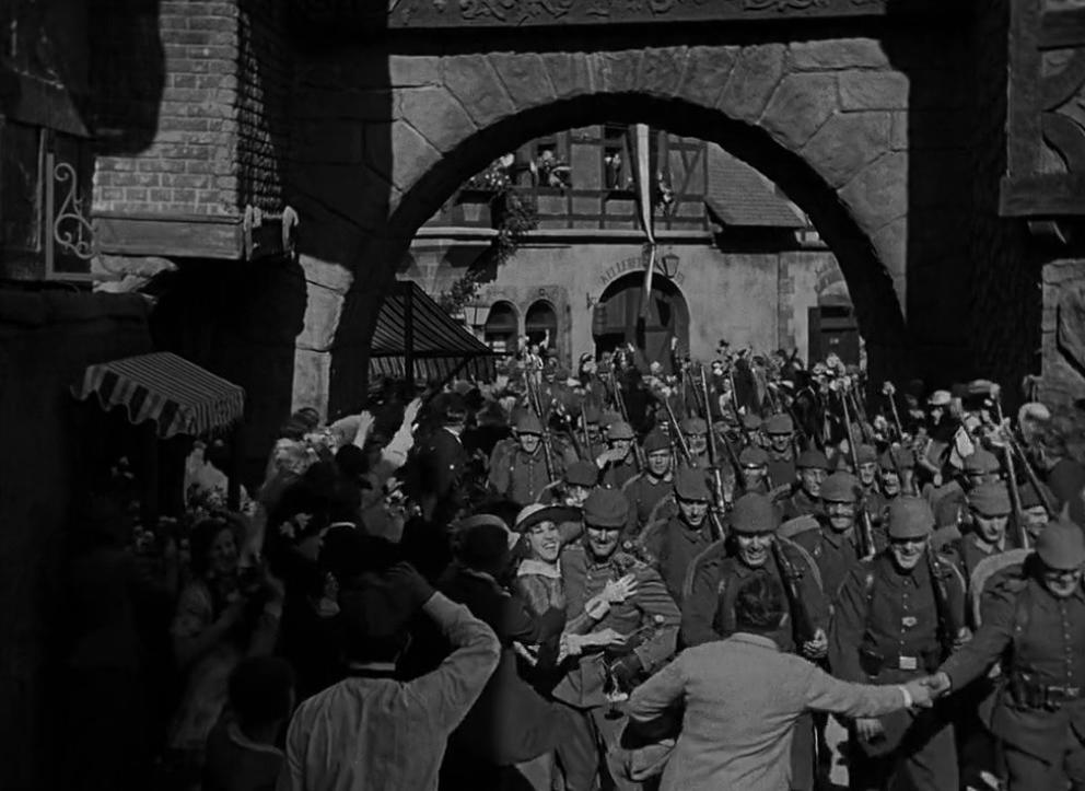 Soldaten marschieren durch ein Tor, während Zivilisten jubeln.