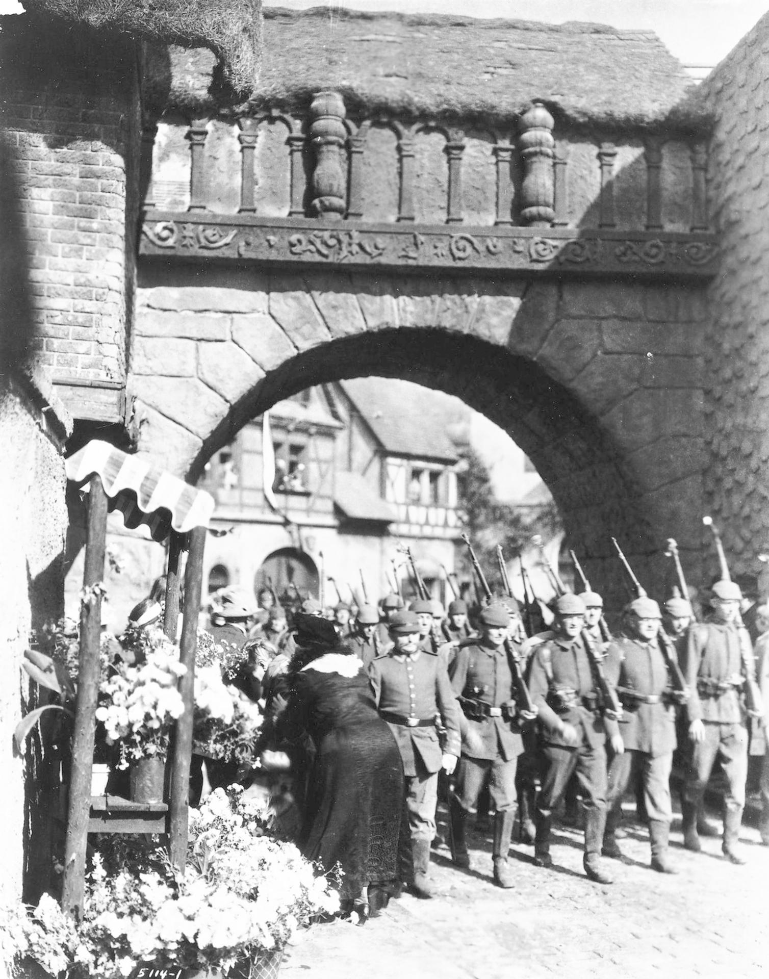 Soldaten marschieren durch ein Tor, Blumen werden dargebracht.